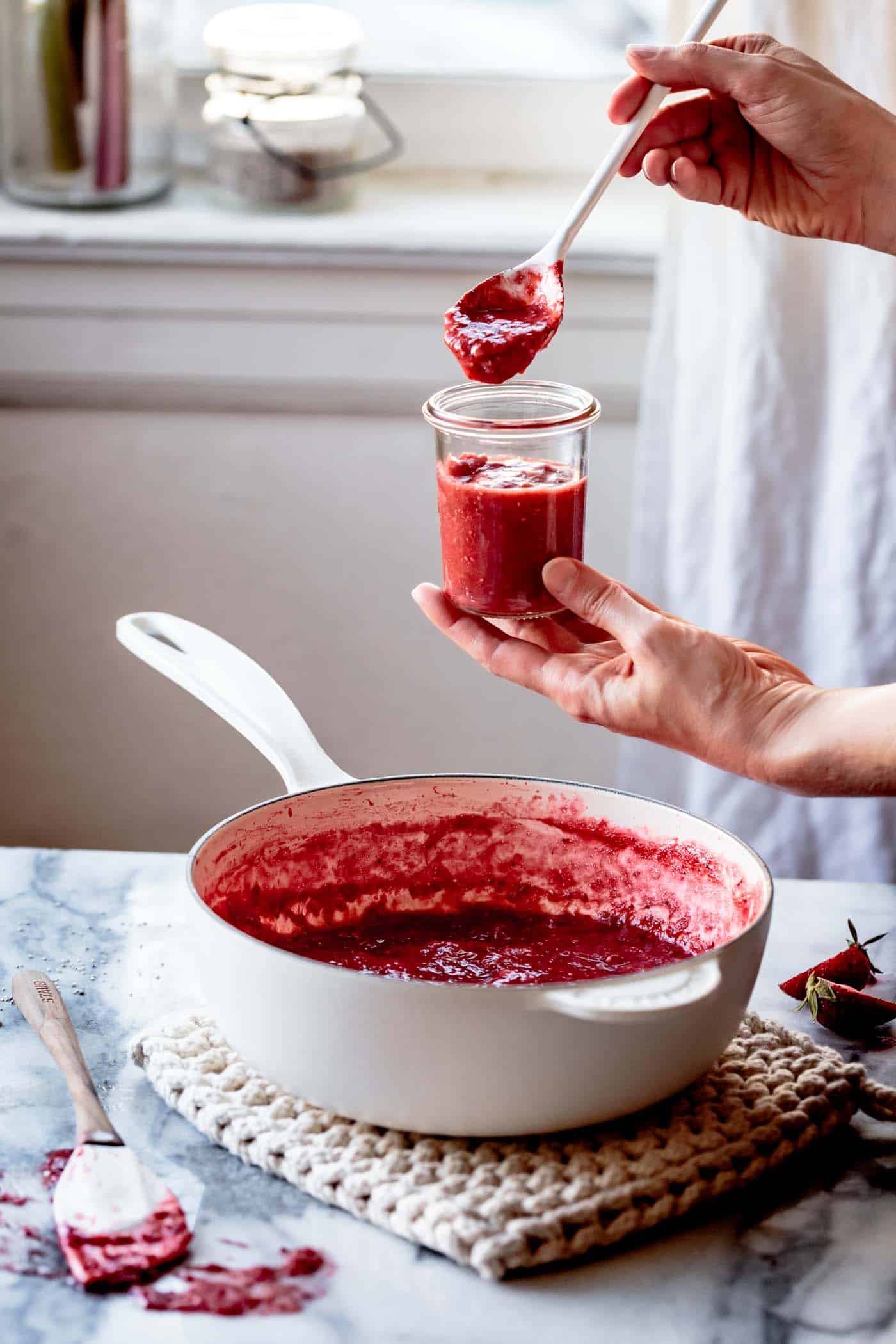 spooning homemade strawberry rhubarb jam into jars
