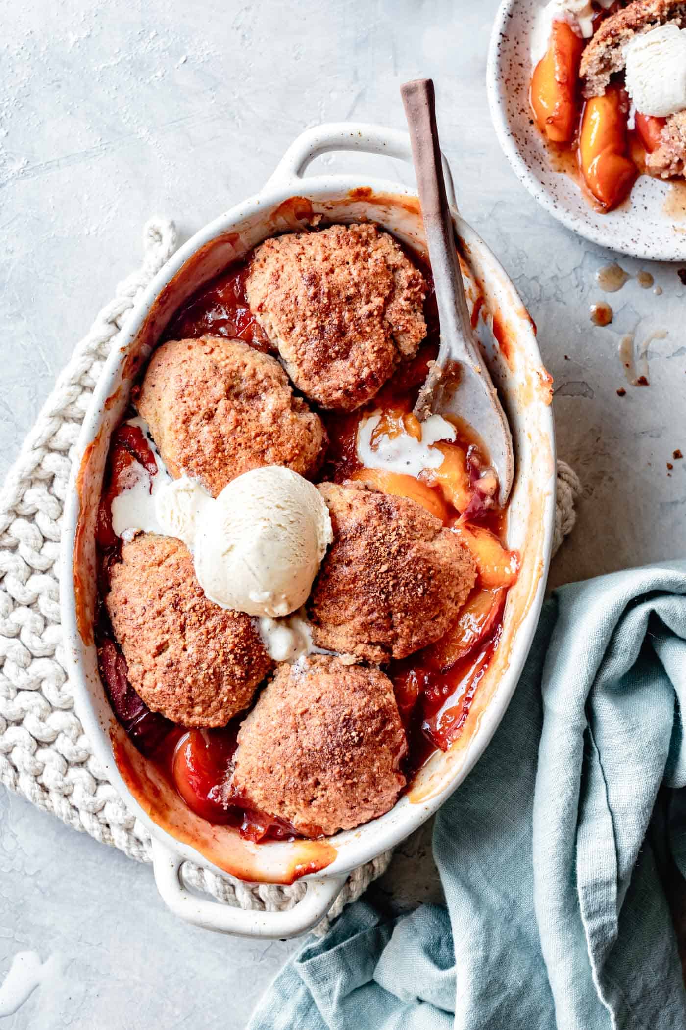 paleo peach cobbler in a white baking dish topped with melty ice cream