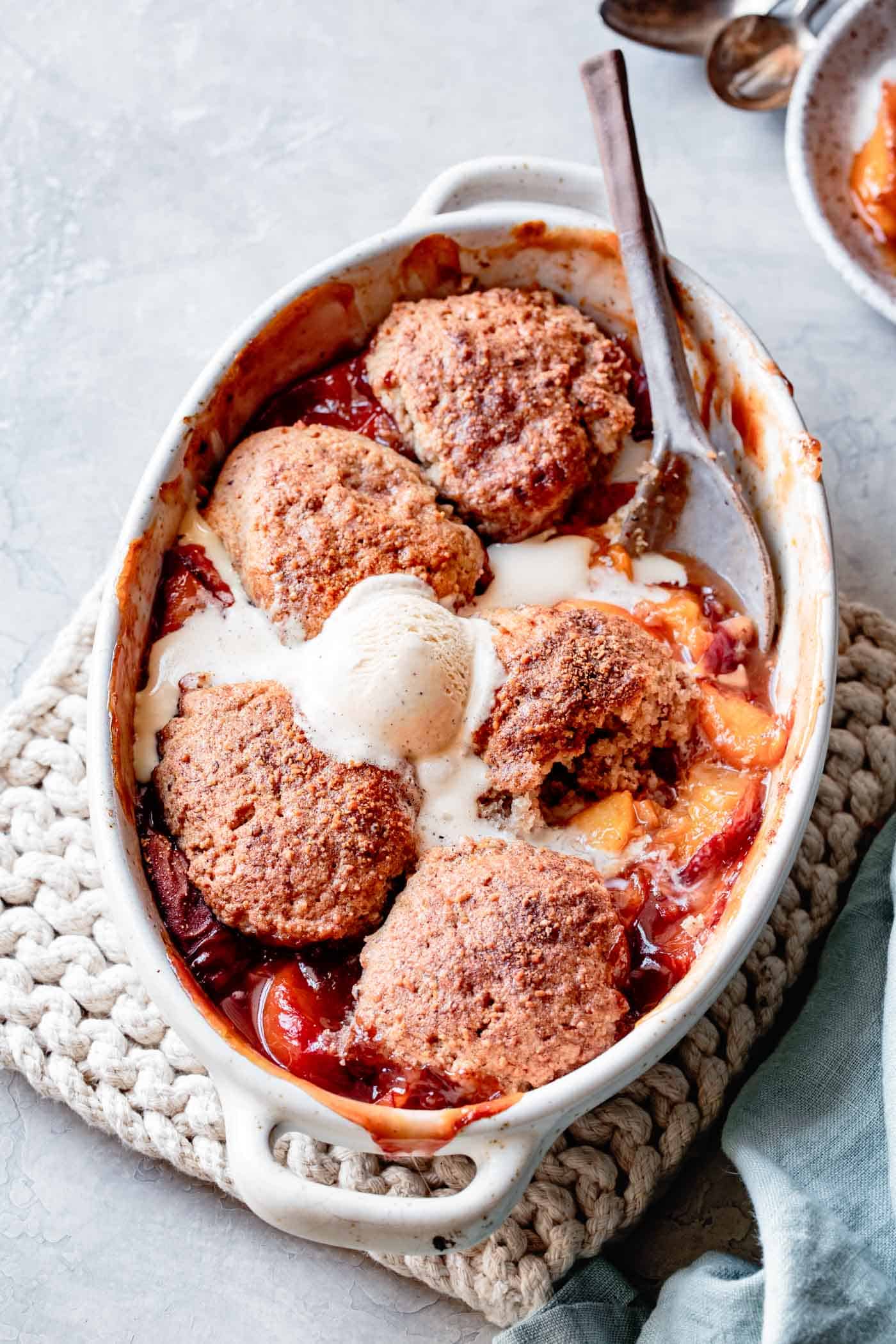 dairy-free peach cobbler recipe, in a baking dish topped with ice cream