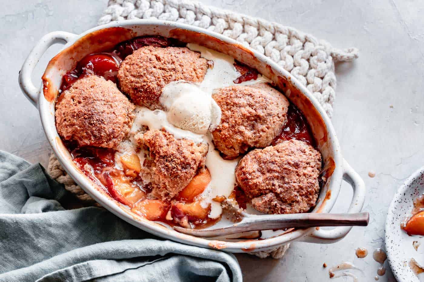 wide image of almond flour peach cobbler topped with melty vanilla ice cream