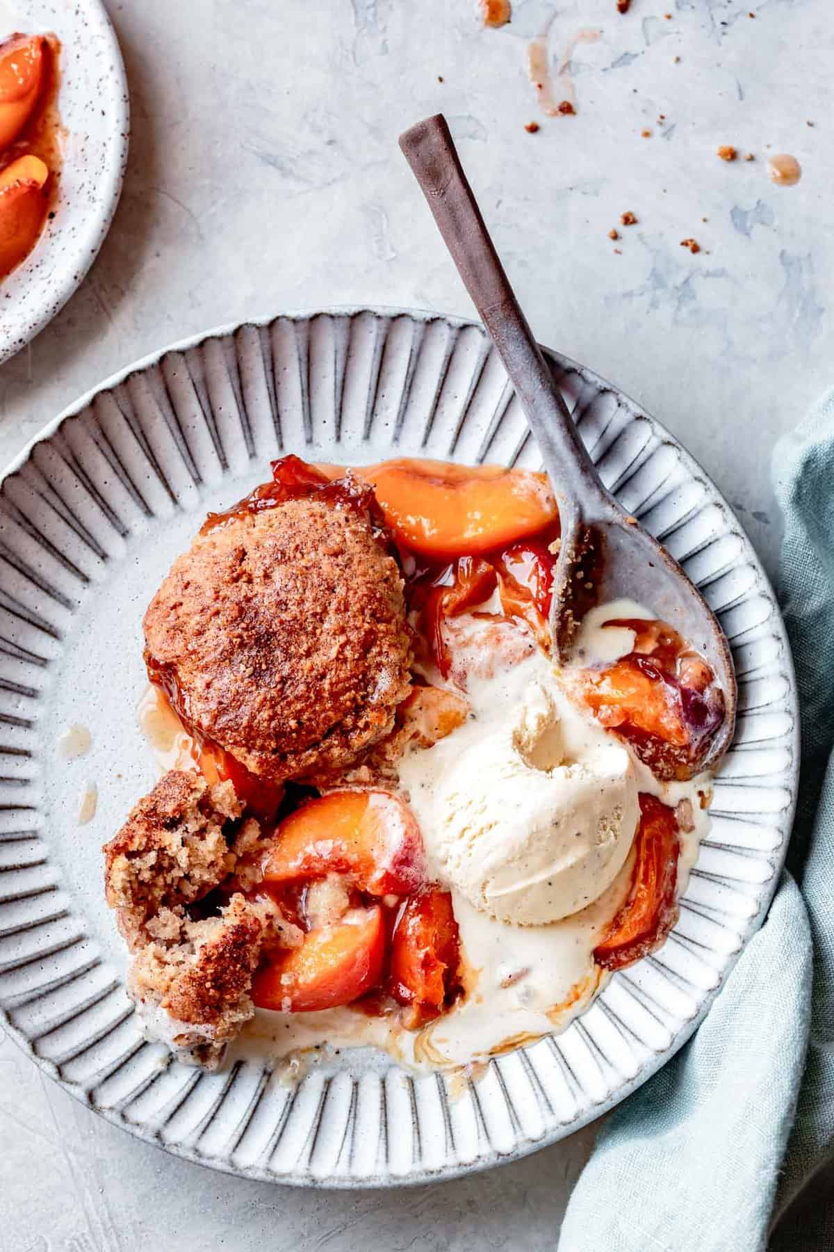 plate of peach almond flour cobbler topped with a scoop of melty ice cream