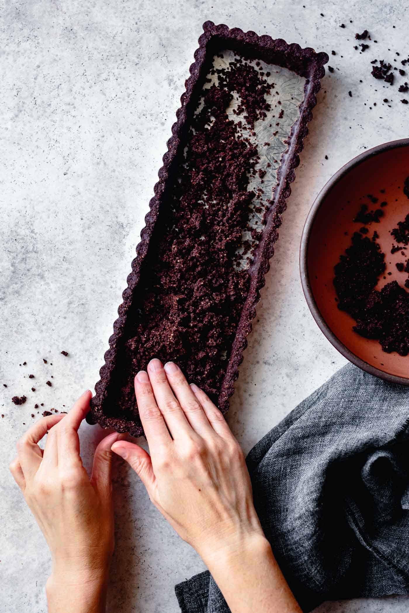 hands pressing cocoa tart crust into pan