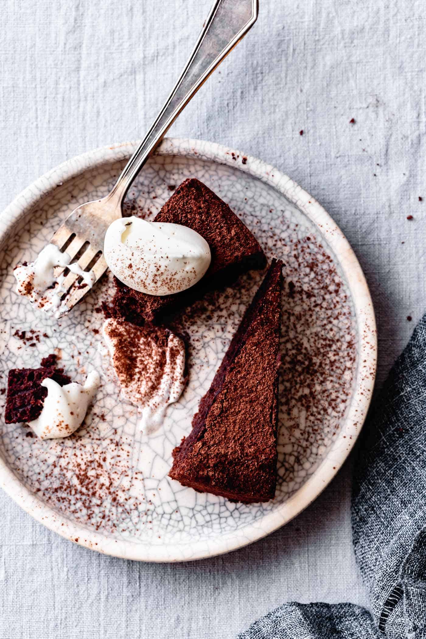 2 slices of chocolate torte on a crackled plate, messy with whipped cream and cocoa and a fork