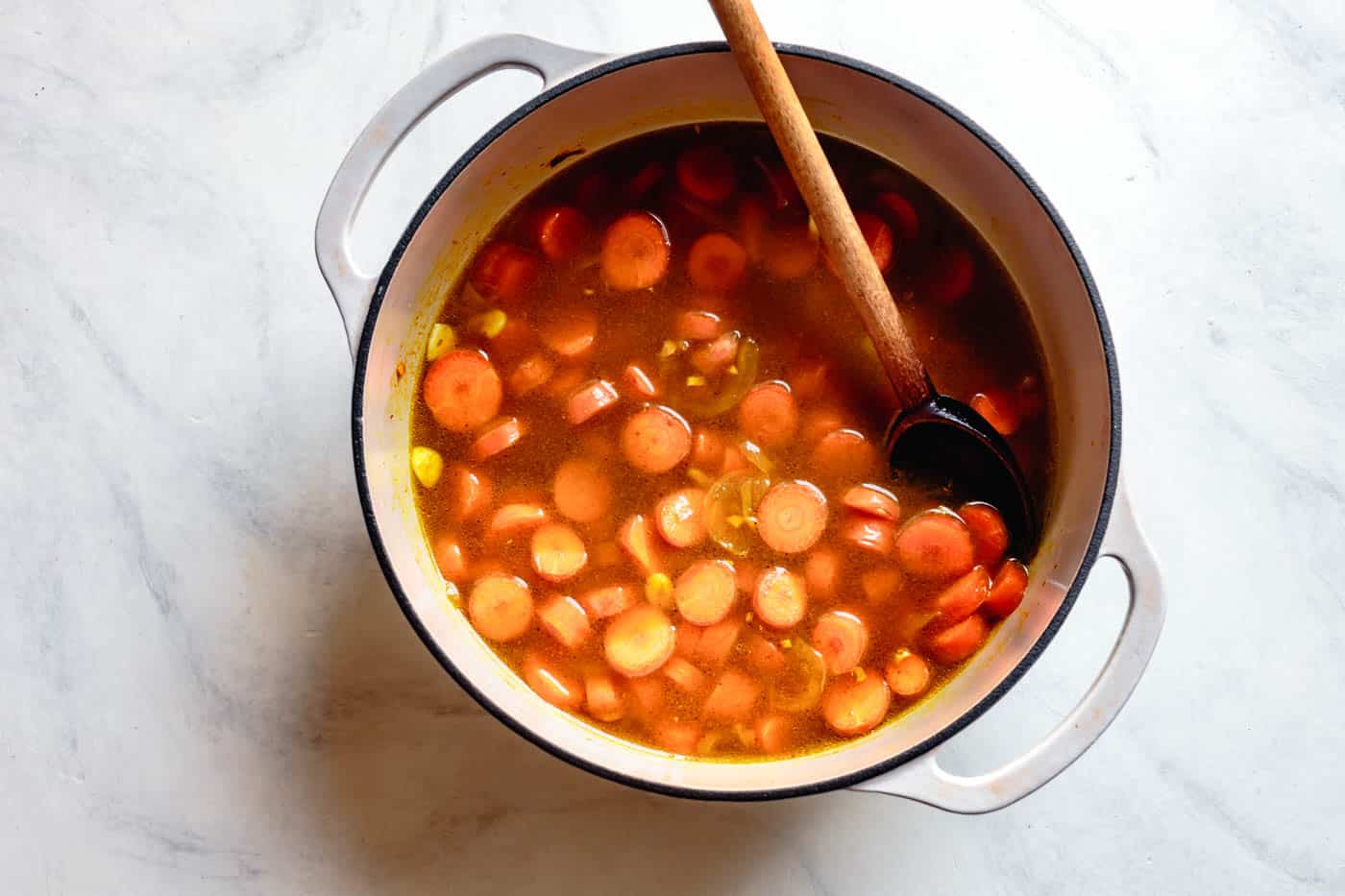 adding stock to recipe for carrot soup with ginger and coconut milk