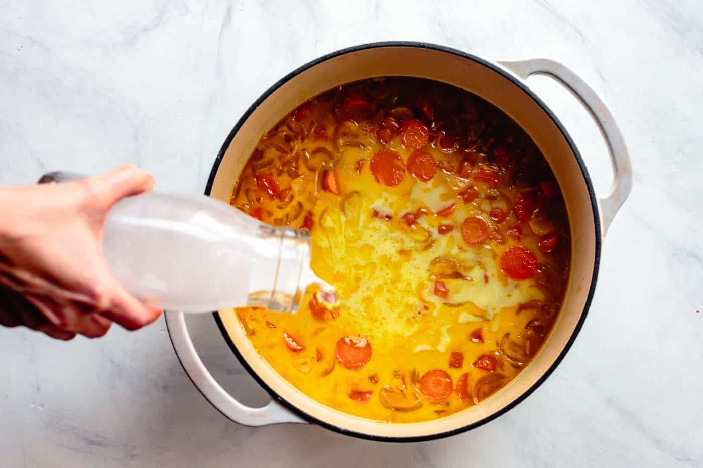 adding coconut milk to curried carrot soup with coconut milk