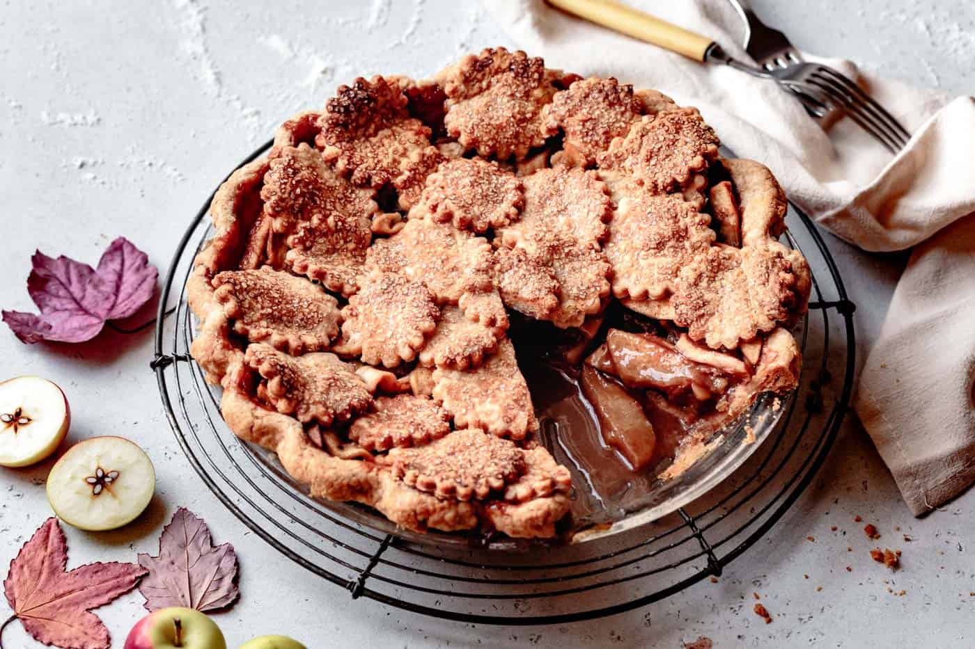 whole gluten-free apple pie with a slice cut out and fall leaves around