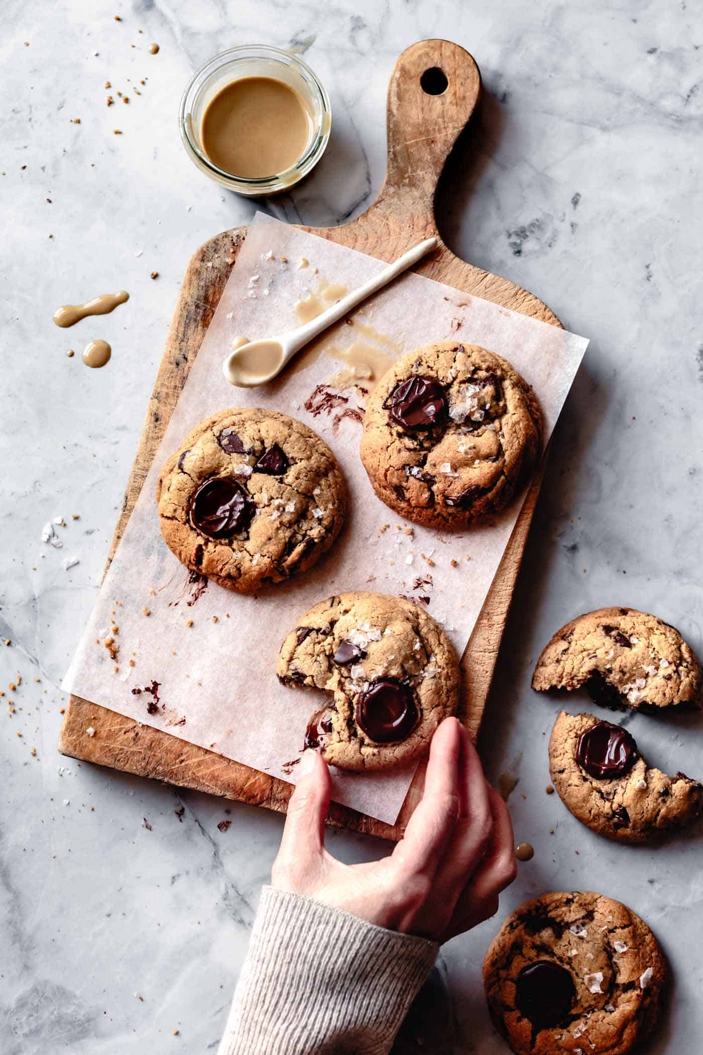 hand grabbing baked chocolate chip cookies with tahini