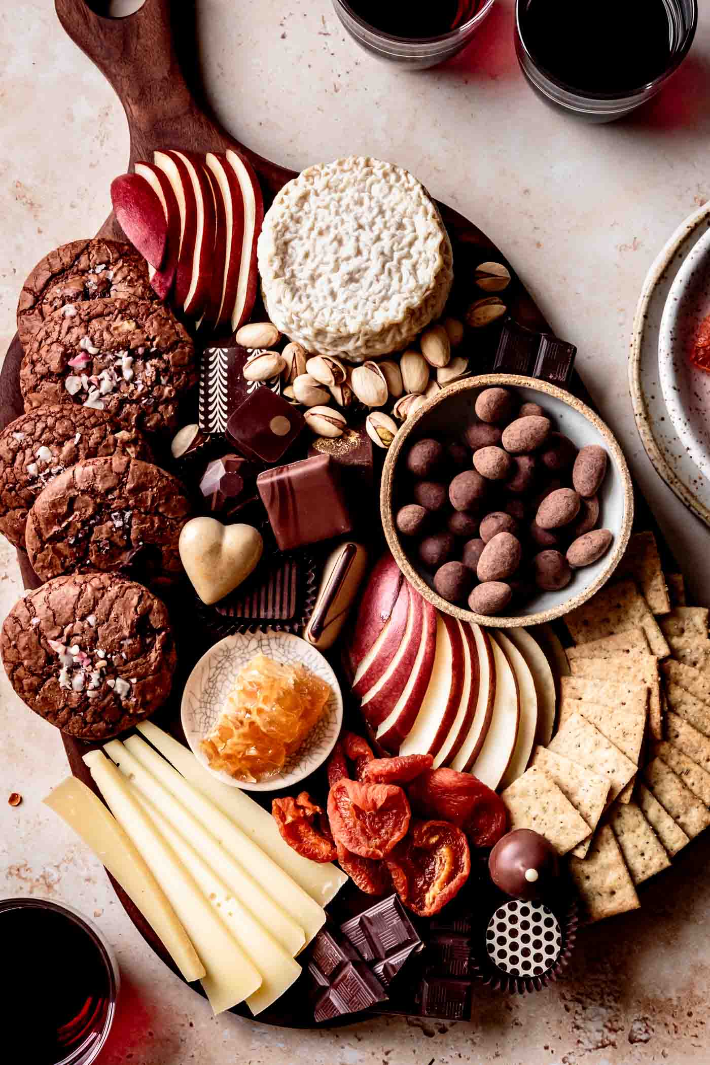 Cheese and chocolate board overhead with red wine in glasses on sandstone surface