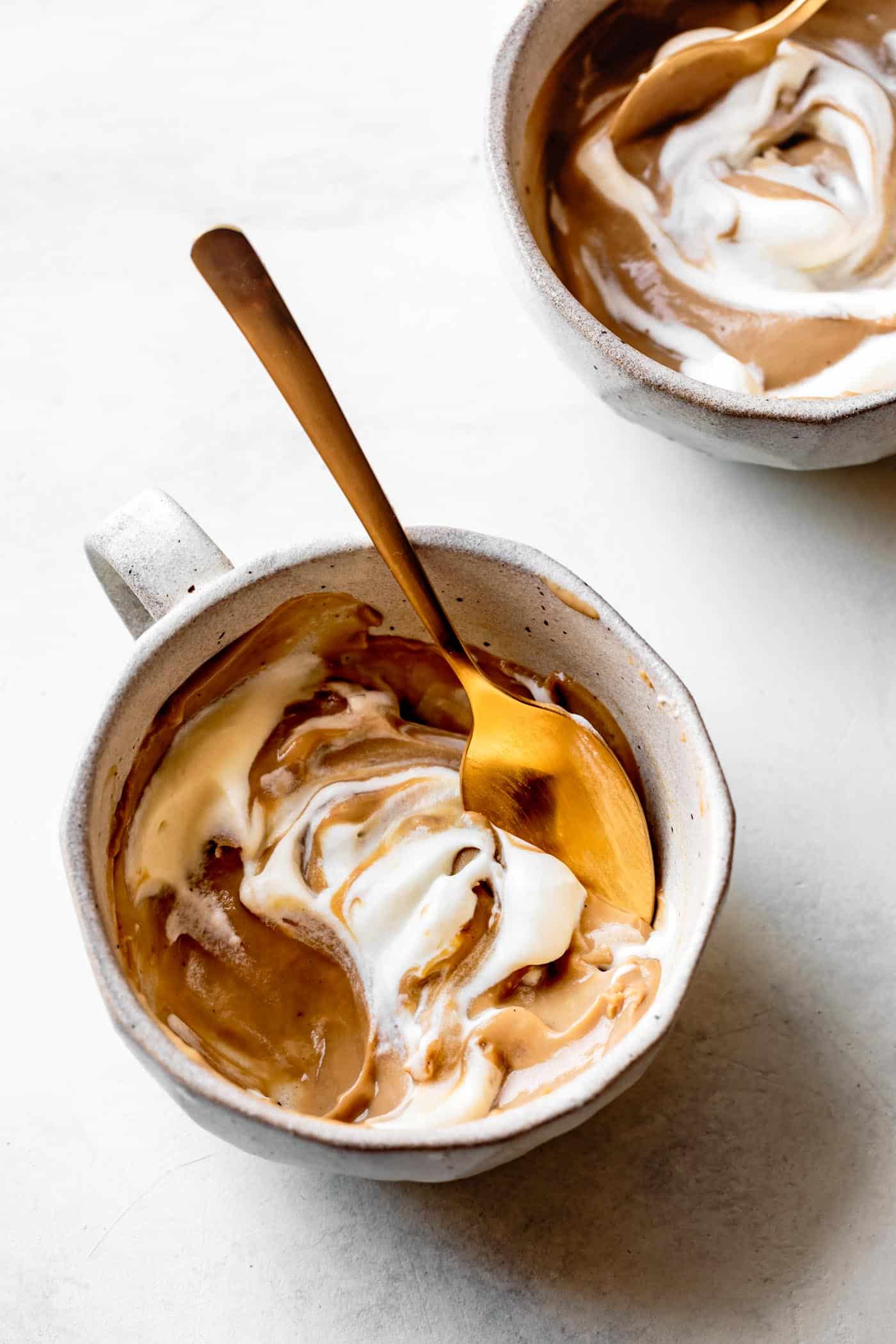 butterscotch pudding in two mugs with whipped cream and a bite taken out