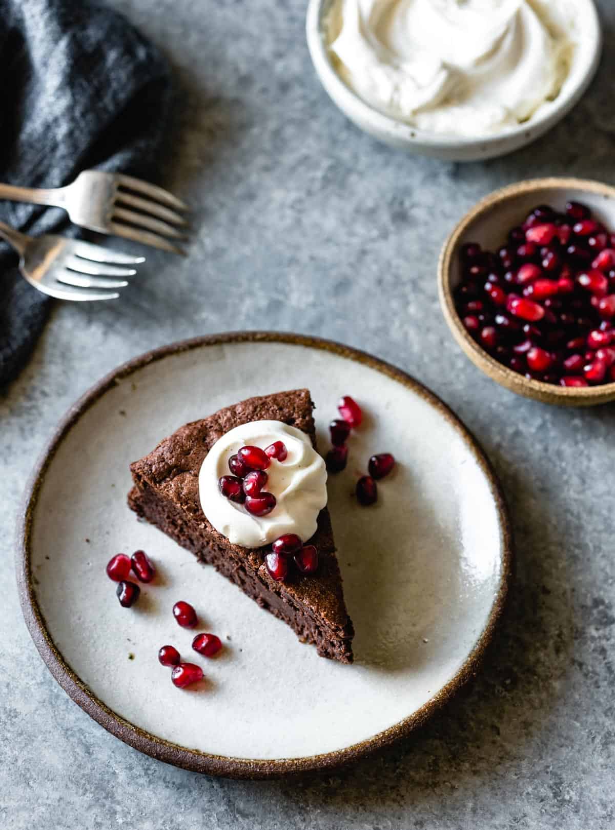 slice of chocolate cake on plate with whipped cream and pomegranates