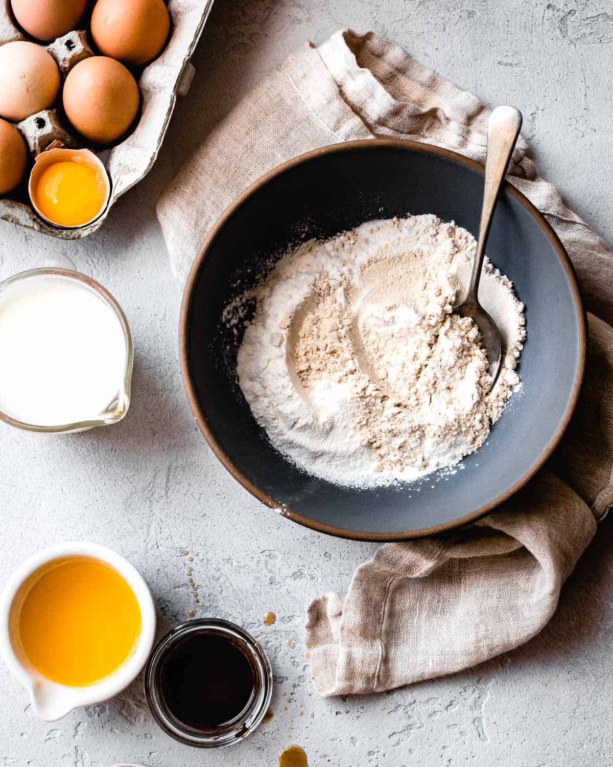 bowl of flour on plaster surface with beige linen, eggs, and other ingredients for passover dessert recipes