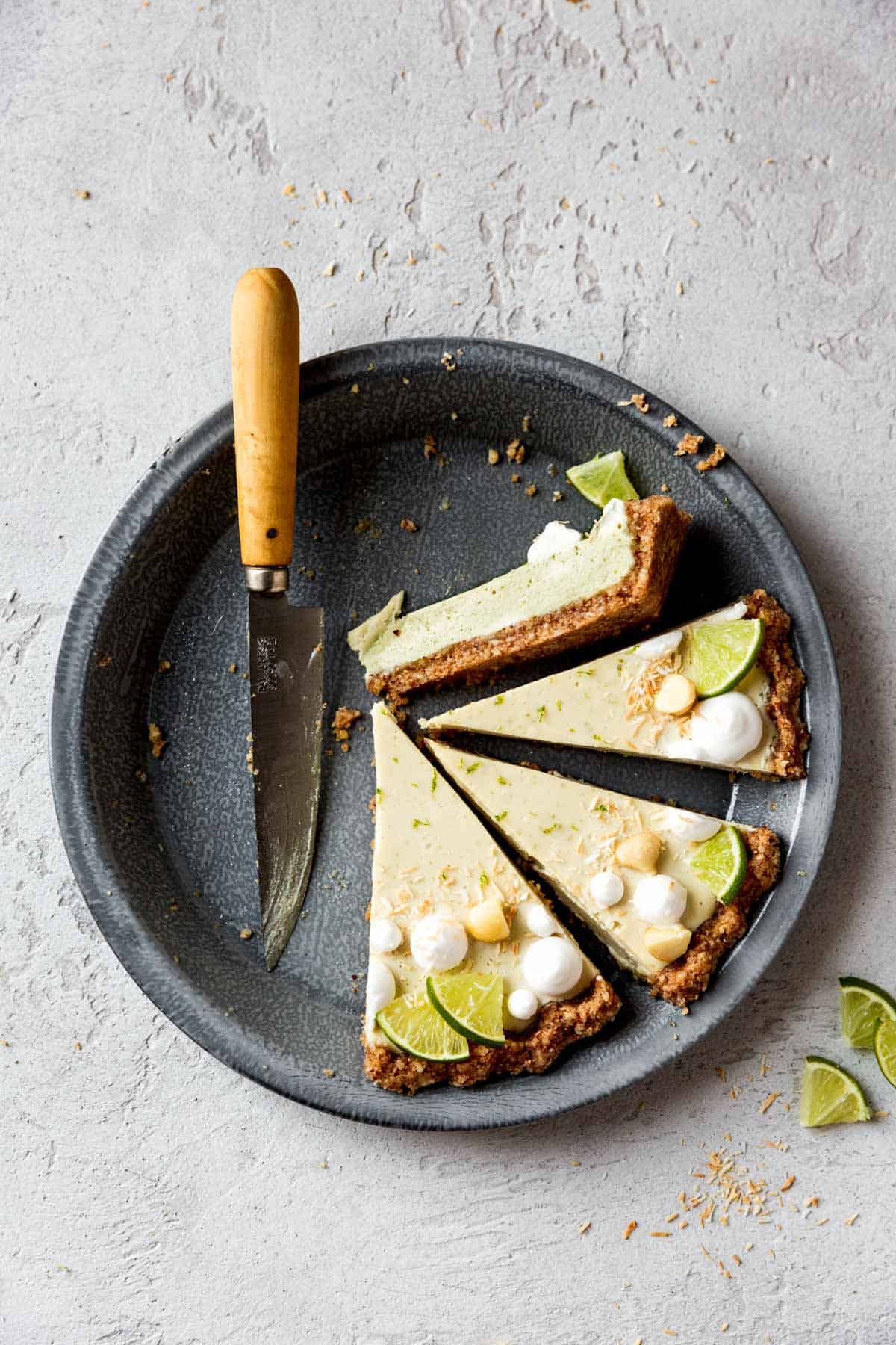 sliced vegan key lime pie in a pie plate on a gray plaster surface