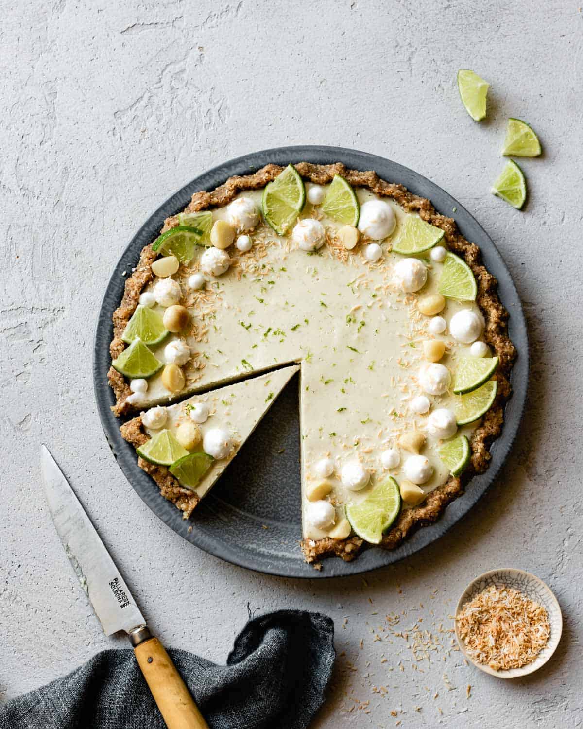 lime tart decorated with lime wedges, coconut, and macadamia nuts, over head on plaster surface