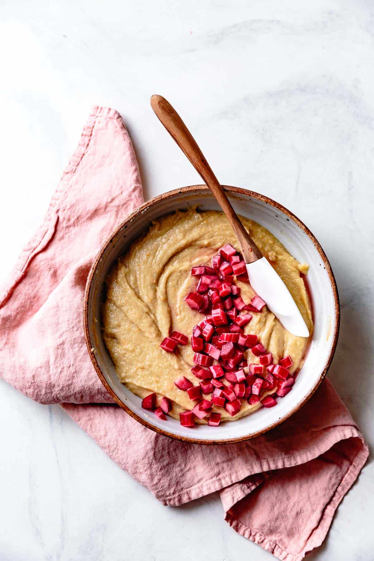 almond cake batter in a bowl with a spatula and rhubarb chunks