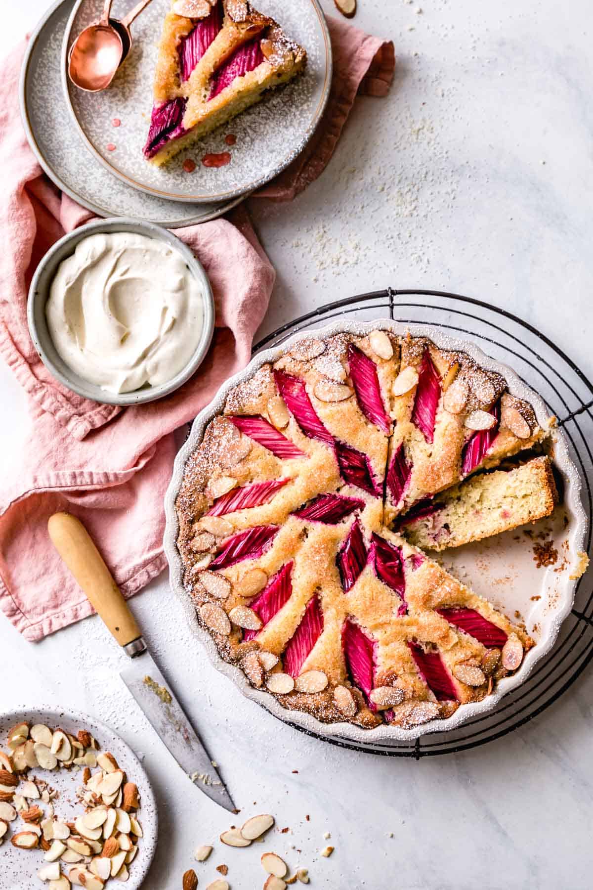 rhubarb almond cake, overhead, with a pink linen, knife, and slices on plates