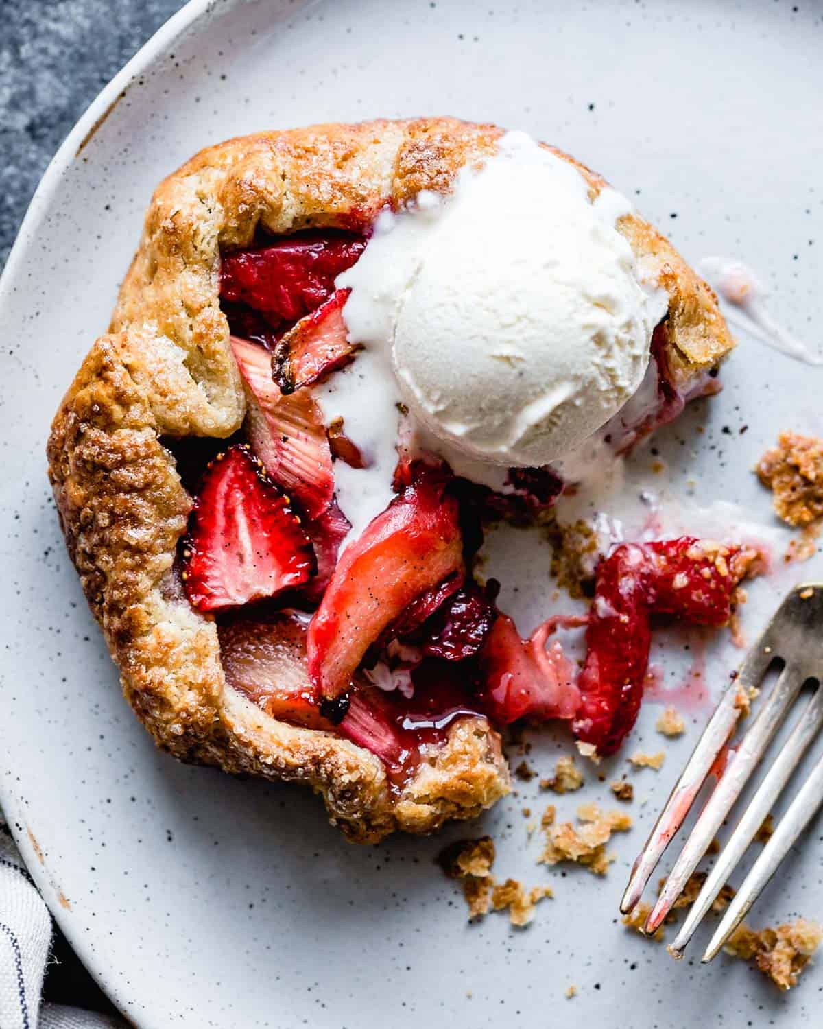 strawberry rhubarb galette topped with melty ice cream with a few bites taken out