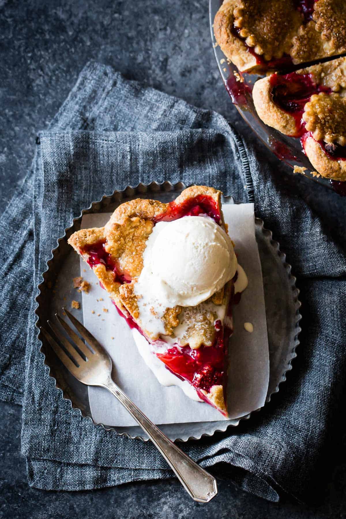berry rhubarb pie slice on a metal plate topped with melty ice cream
