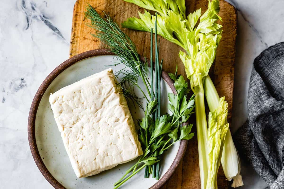 tofu on a plate with whole herbs and celery on a board