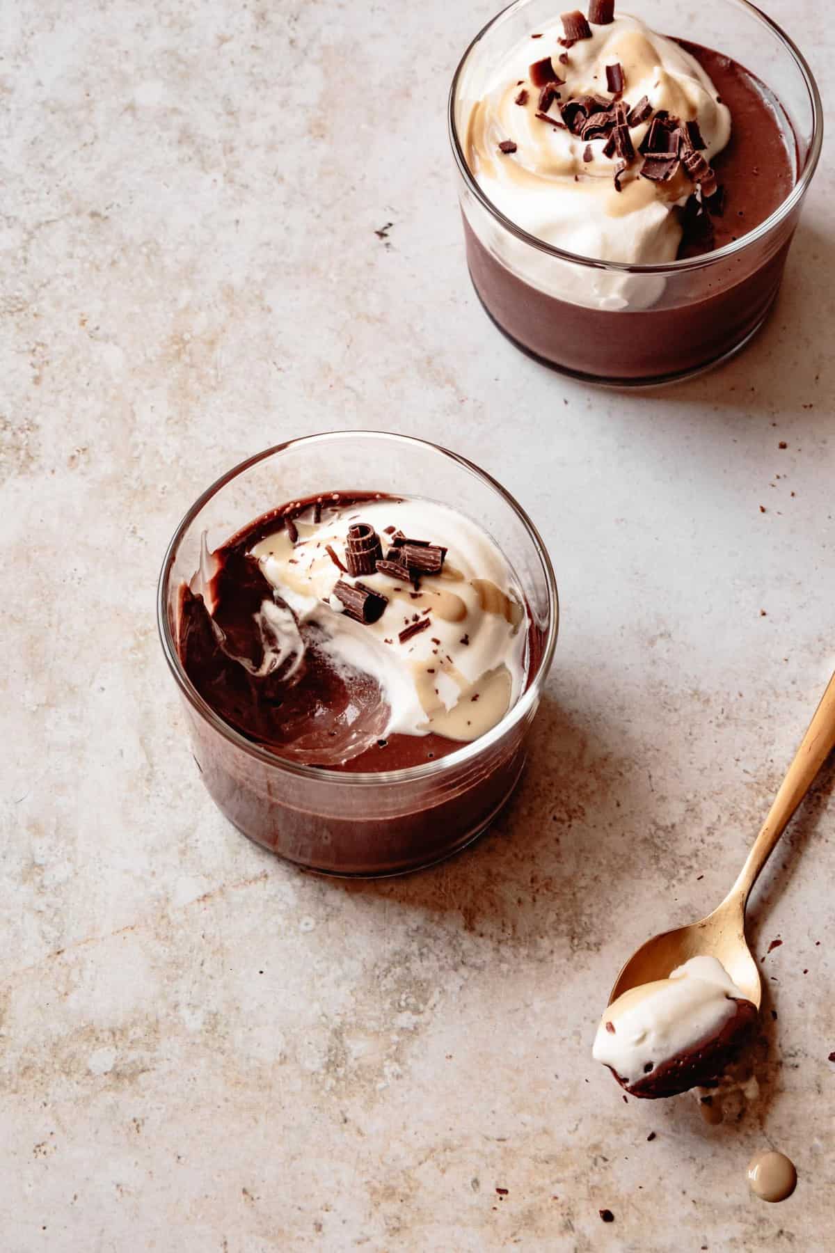 two glasses of vegan chocolate pudding on a surface with a spoonful taken out