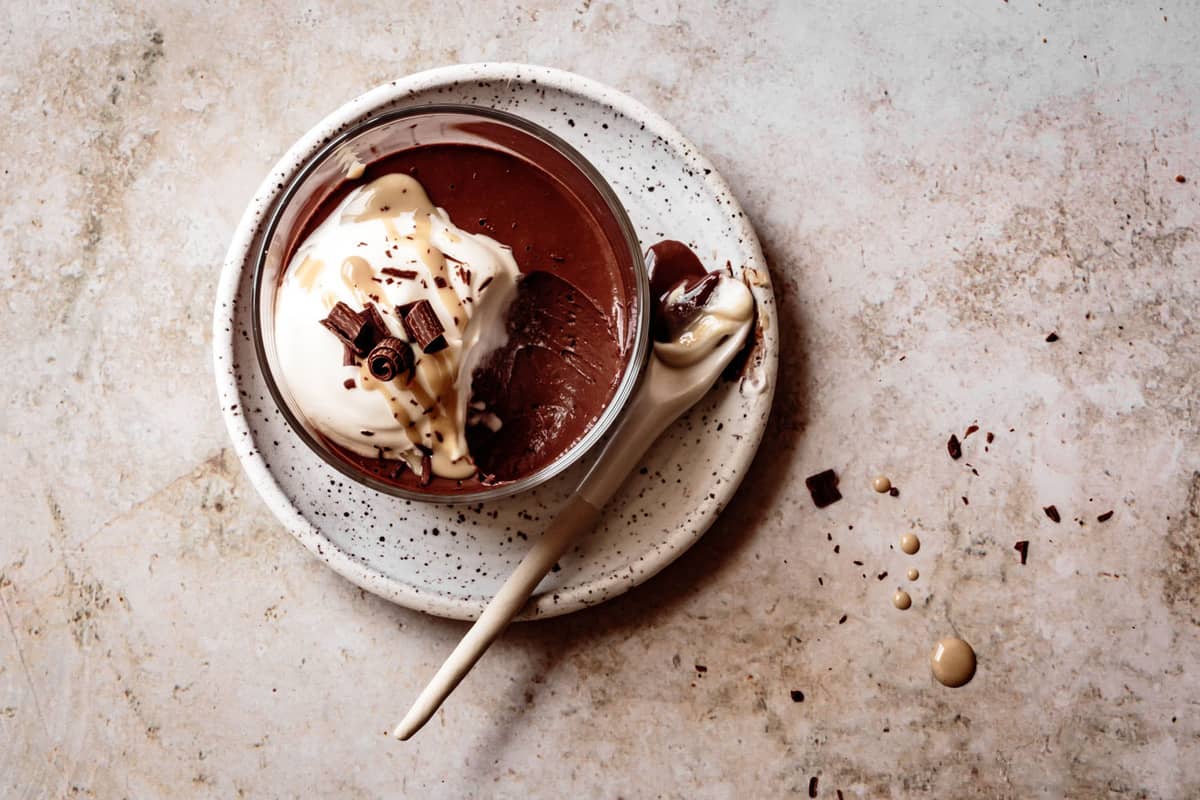 healthy chocolate pudding in a glass on a small plate with a ceramic spoon