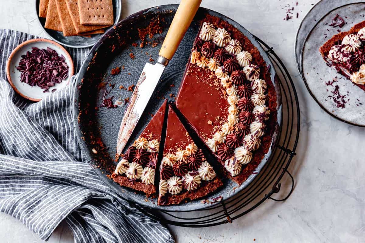 vegan chocolate cream pie, partially sliced in a blue vintage pan with striped linen and knife