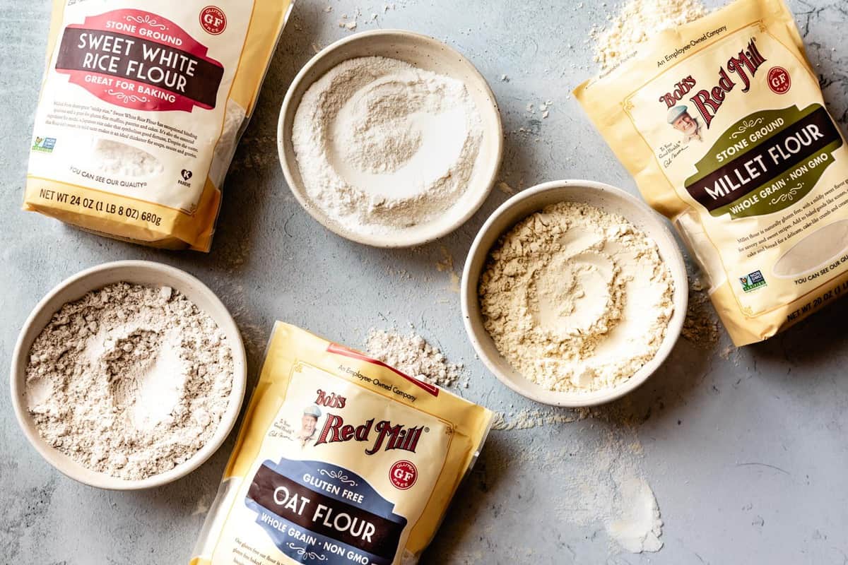 a trio of flours are shown on a gray surface: sweet rice flour, millet flour, and oat flour