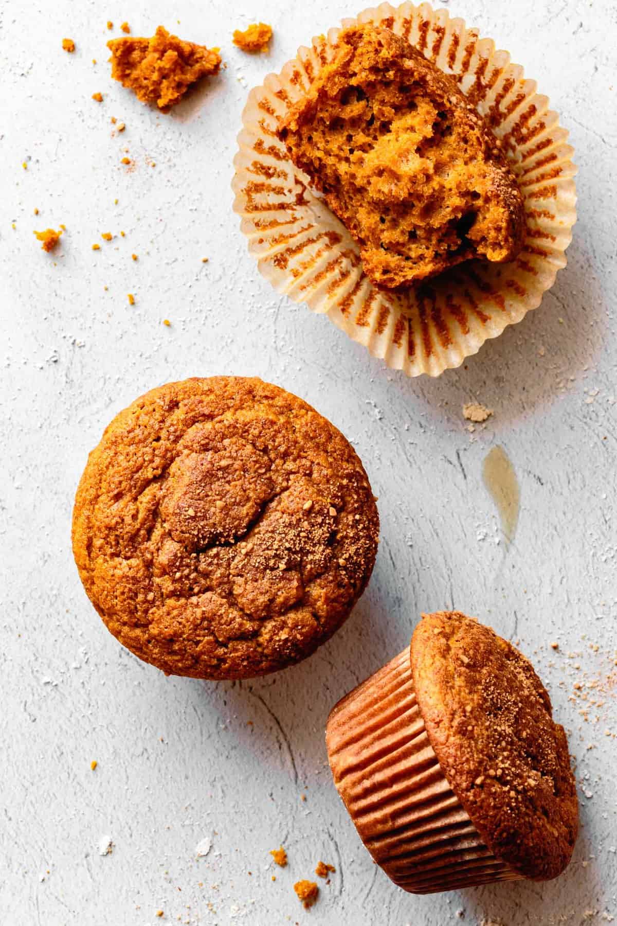 overhead of three healthy gluten-free pumpkin muffins in various stages of disaray