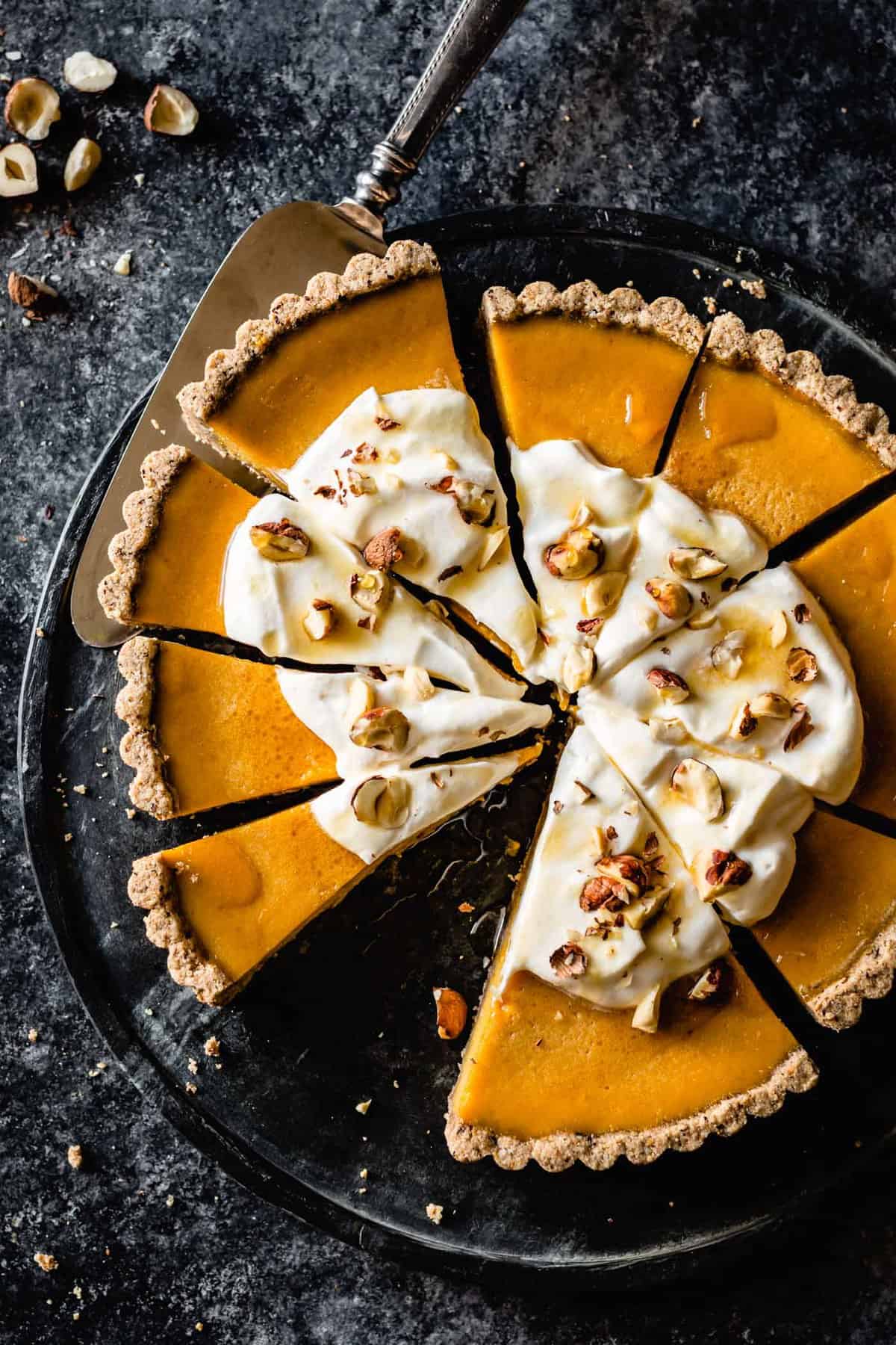 vibrant orange pumpkin tart, sliced and topped with whipped cream and hazelnuts on a black marble platter