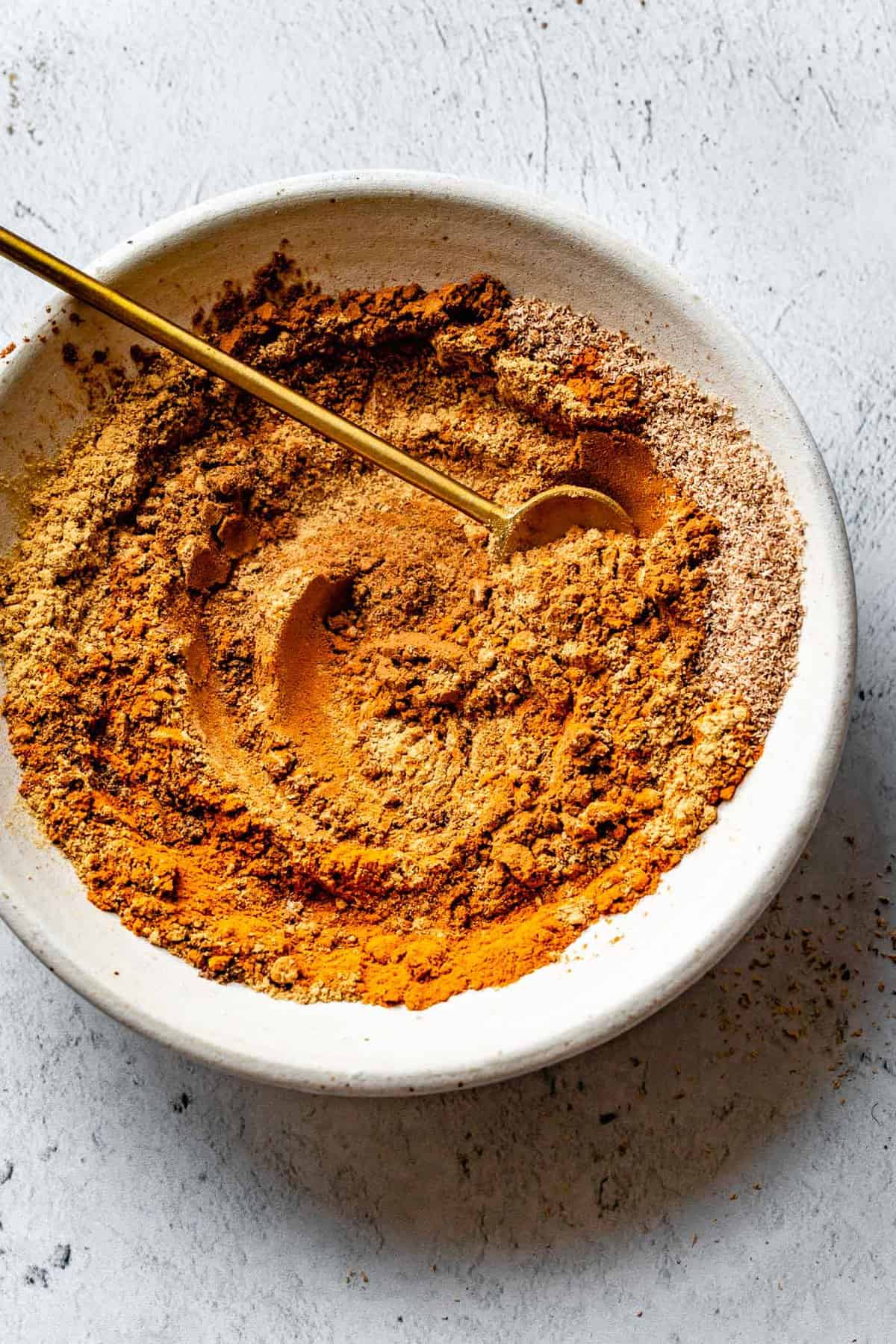 pumpkin spice mix swirled in a white bowl with a brass spoon