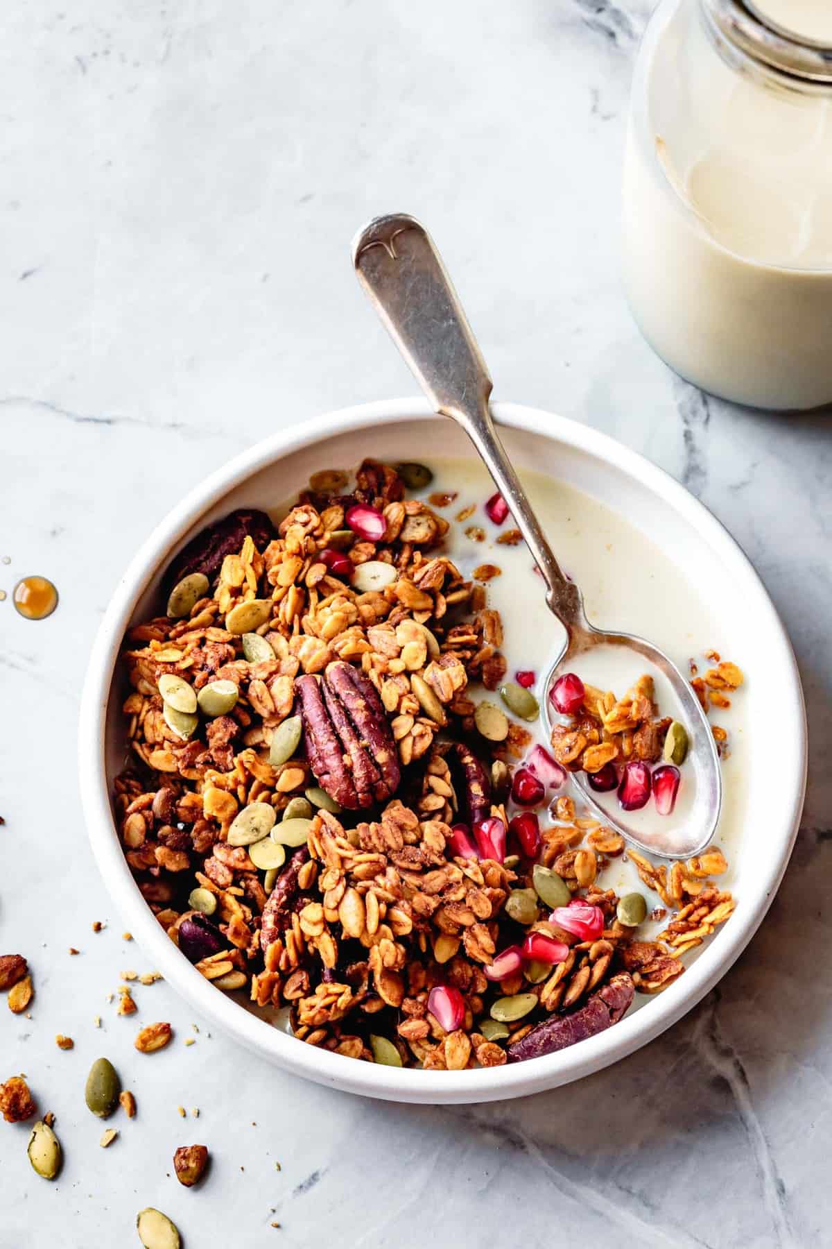 pumpkin spice granola in a white bowl with milk and pomegranate arils