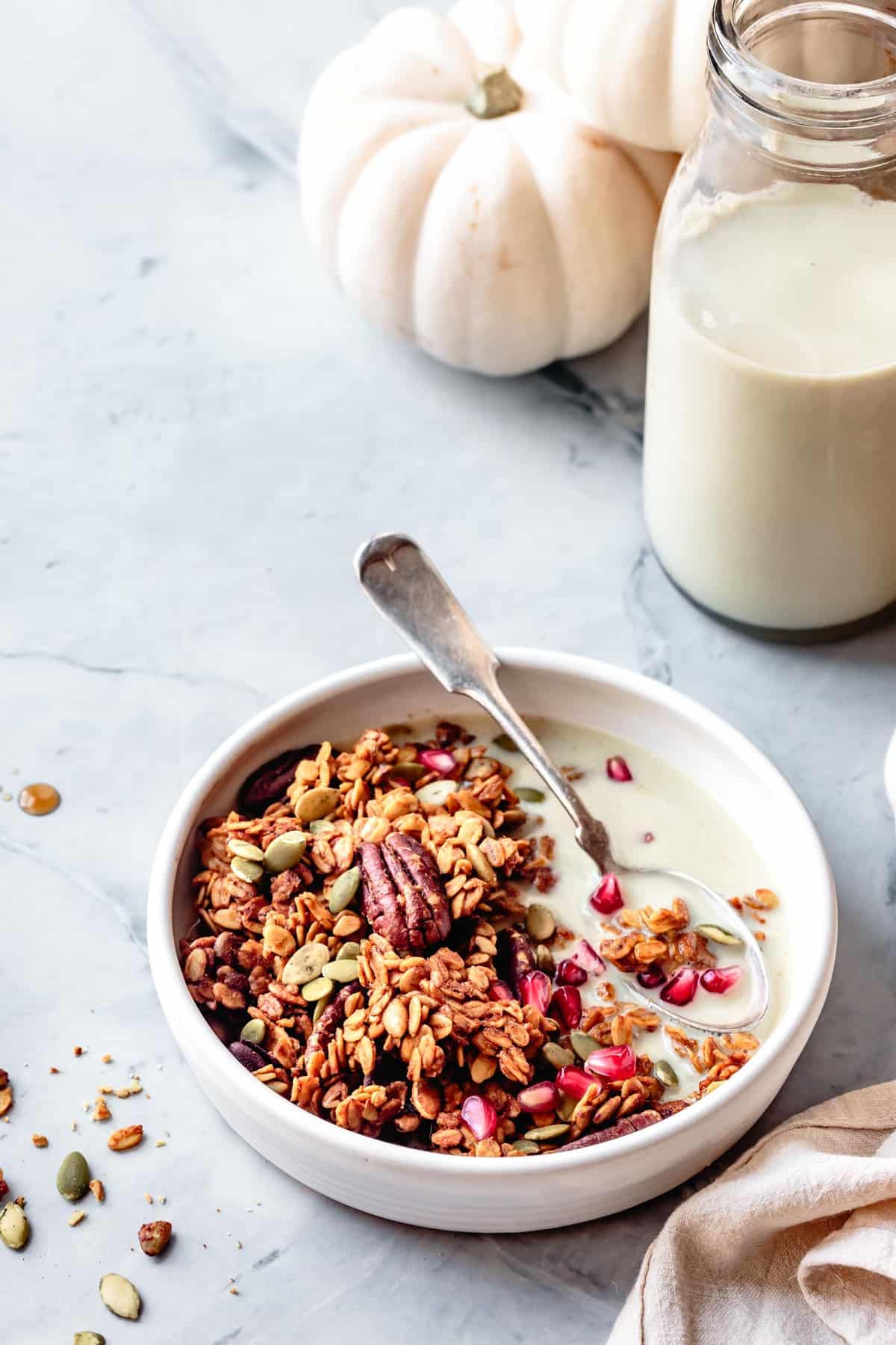 pumpkin seed granola in a bowl with a jar of milk and white mini pumpkins in the background