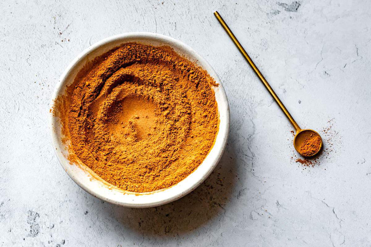 golden pumpkin pie spice in a white bowl with a brass spoon