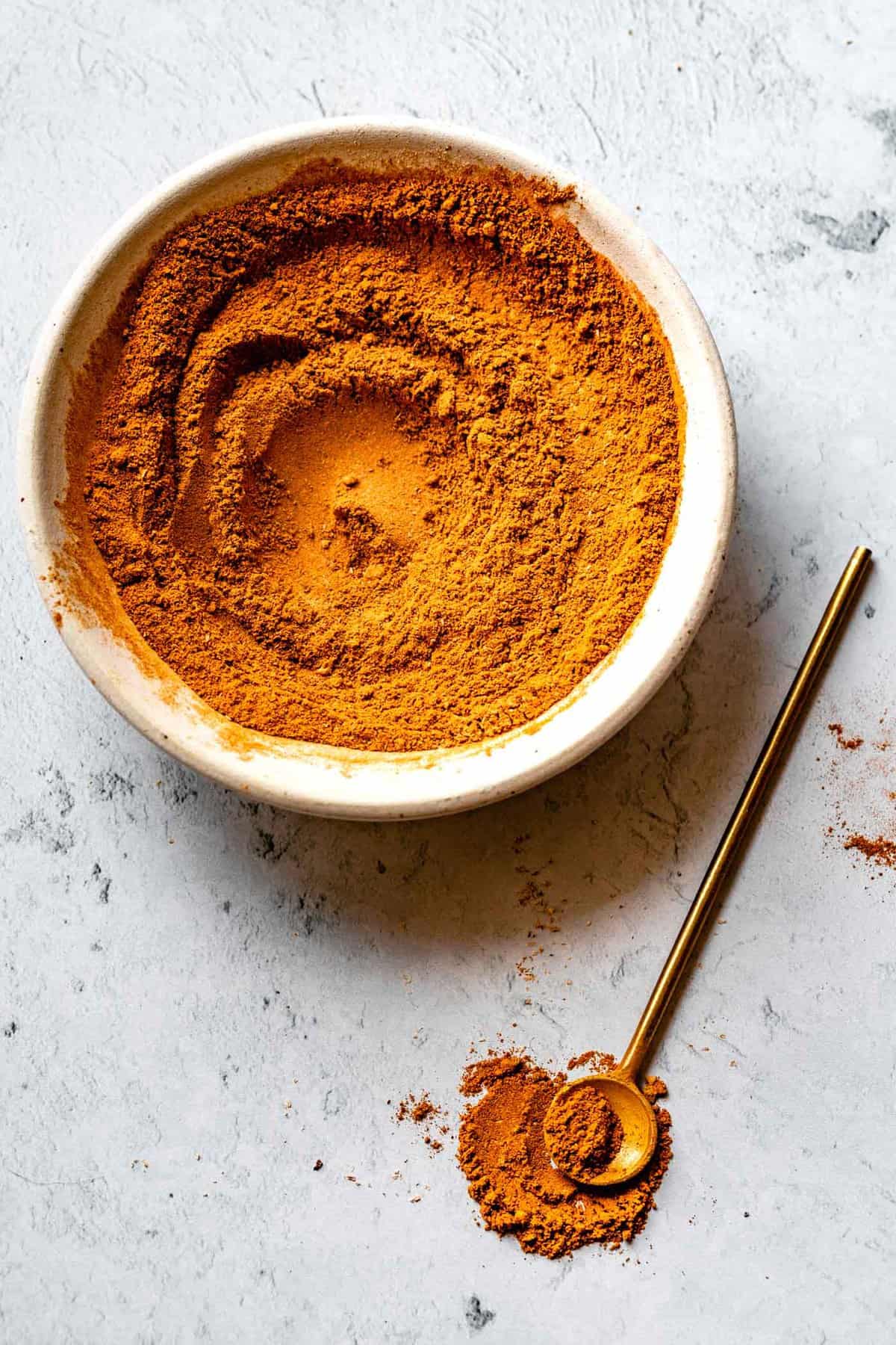golden pumpkin spice mix in a white bowl with a brass spoon