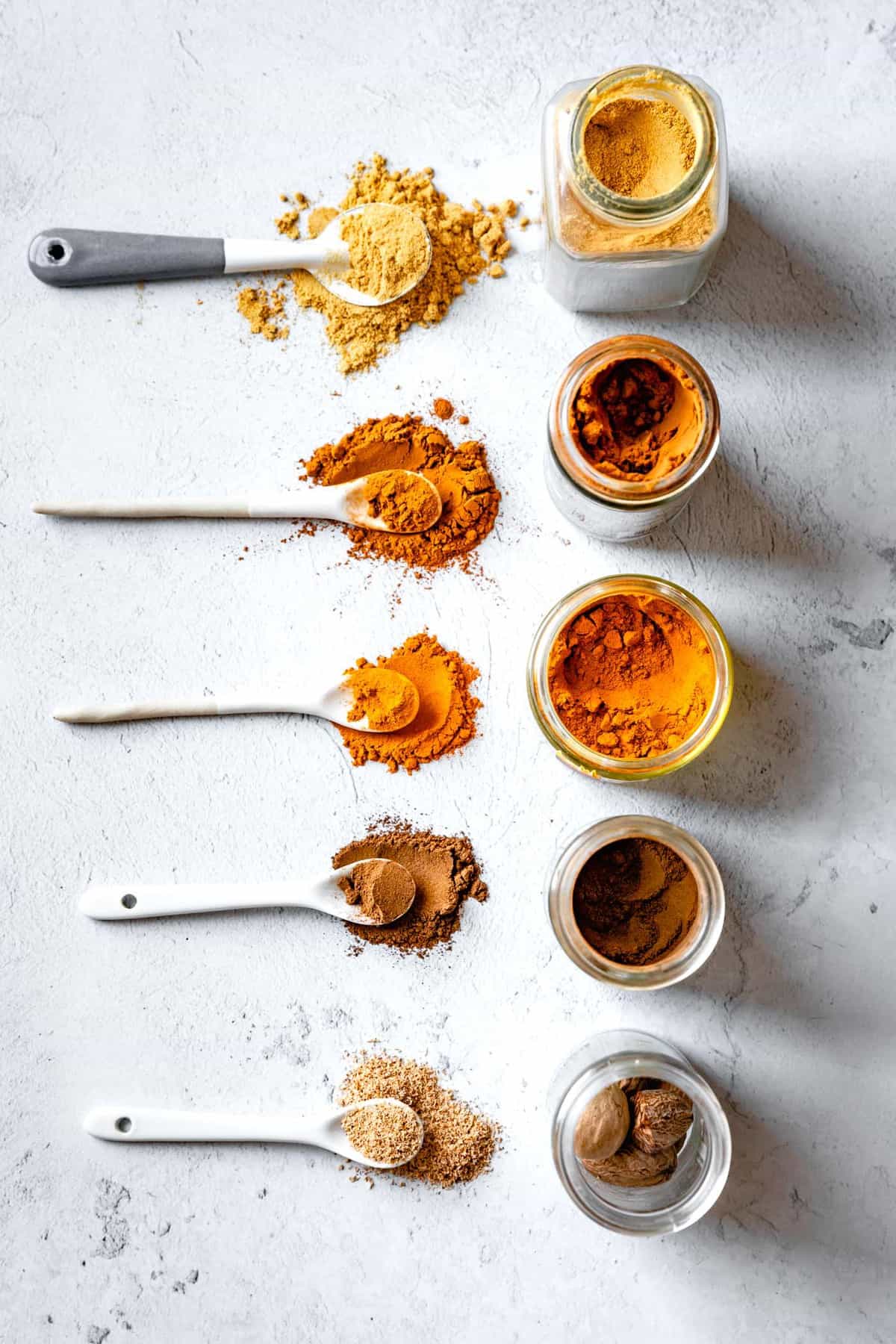 ground spices in jars and small white spoons in two lines for DIY pumpkin pie spice