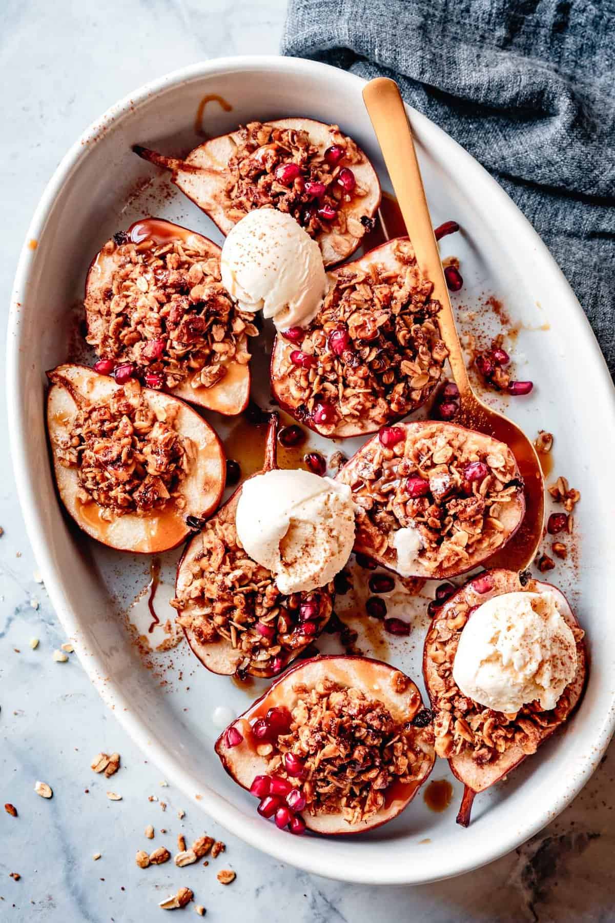 eight roasted pear halves in an oval dish topped with sauce and ice cream