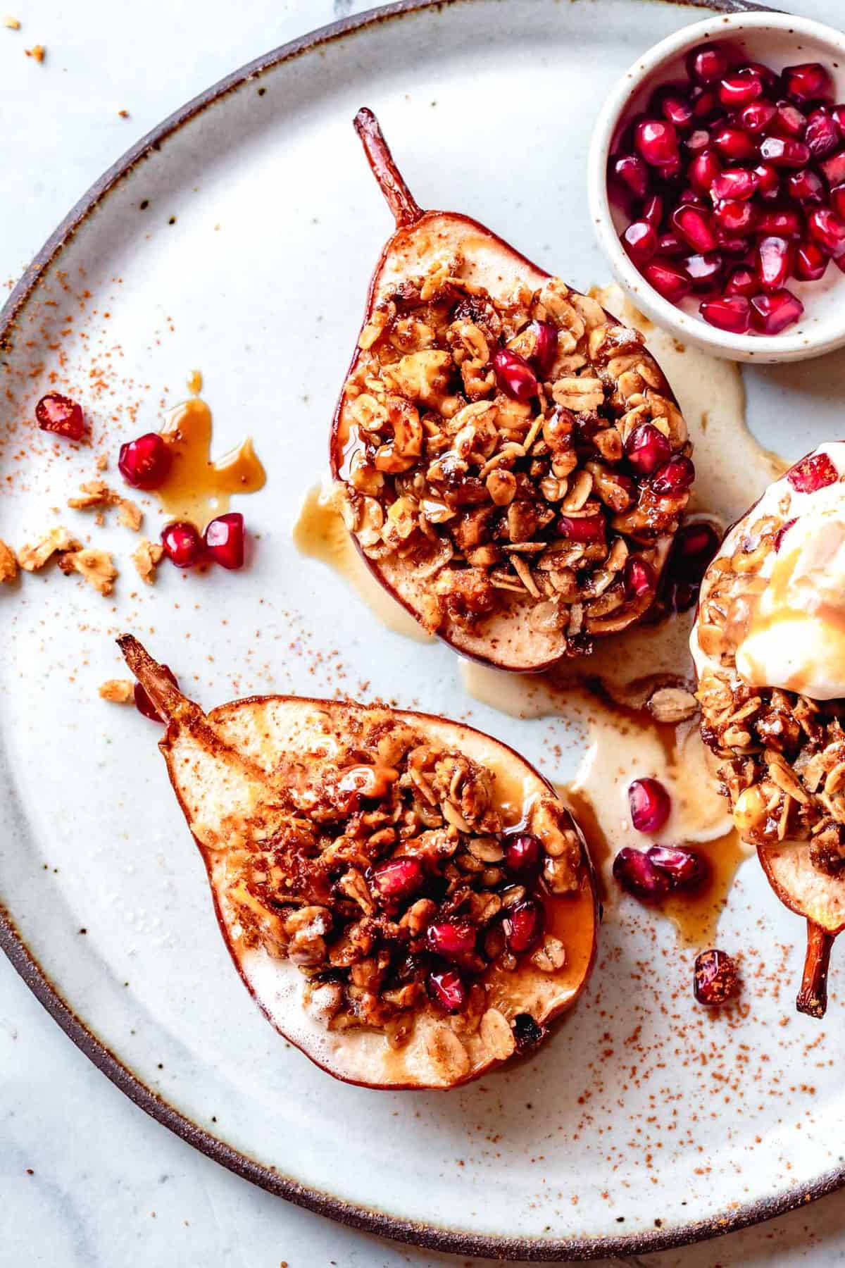 overhead of roasted pears on a plate with melty ice cream, pomegranates, and sauce