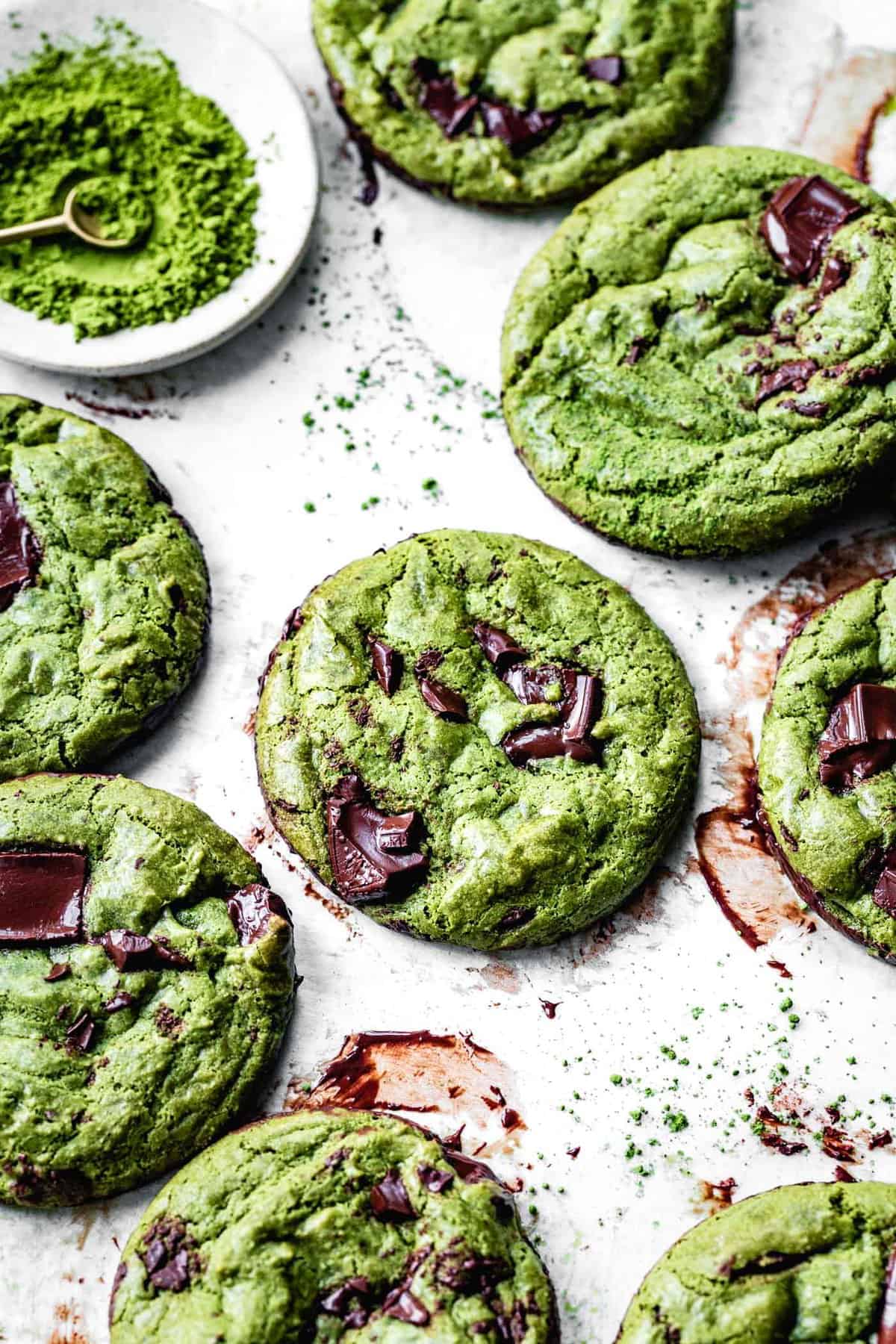 several green cookies are on a messy piece of parchment smeared with chocolate