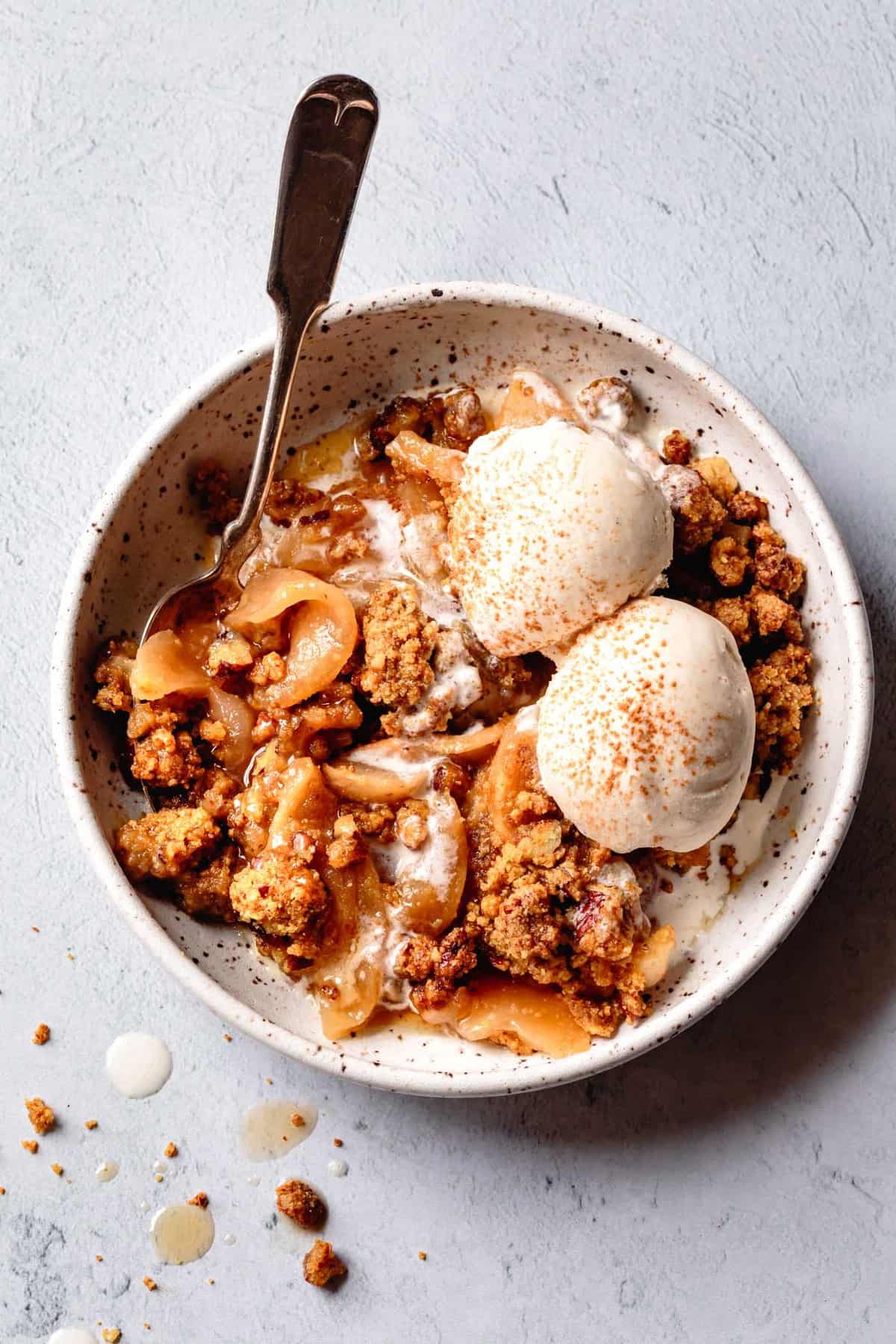 paleo apple crisp in a bowl topped with scoops of ice cream dusted with cinnamon