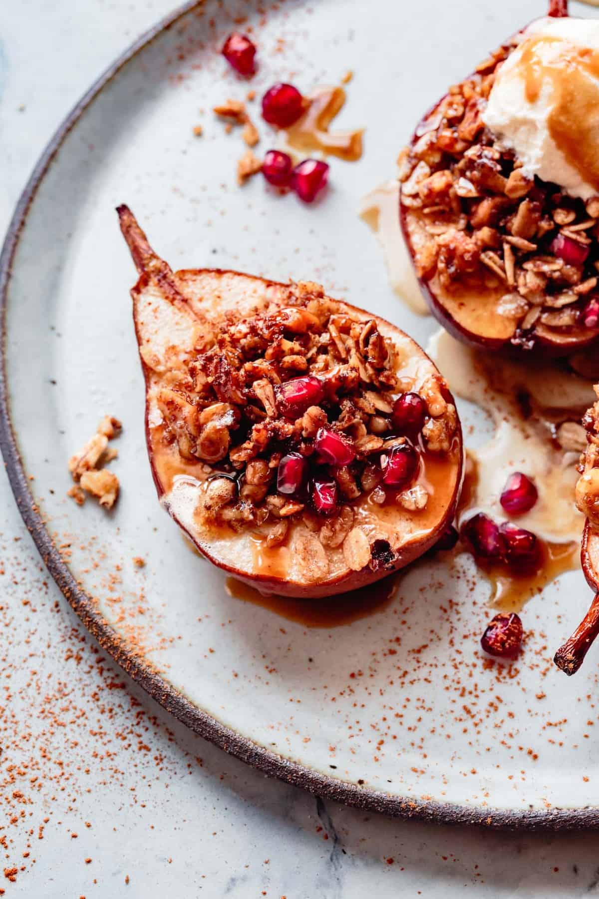 close up of roasted pear on a plate filled with oat crumble and pomegranate arils