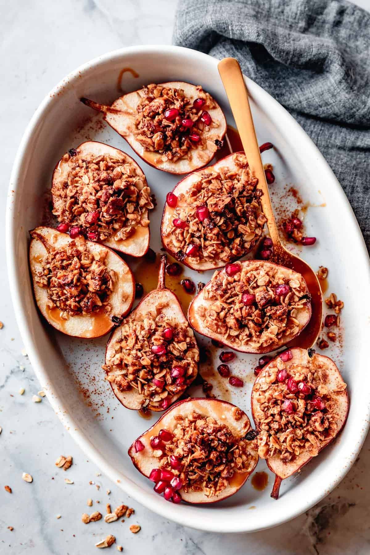 stuffed pears in a white oval pan with a gold spoon