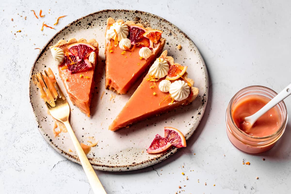 three blood orange tart slices on a speckled plate with a gold fork, bites taken out of the slices
