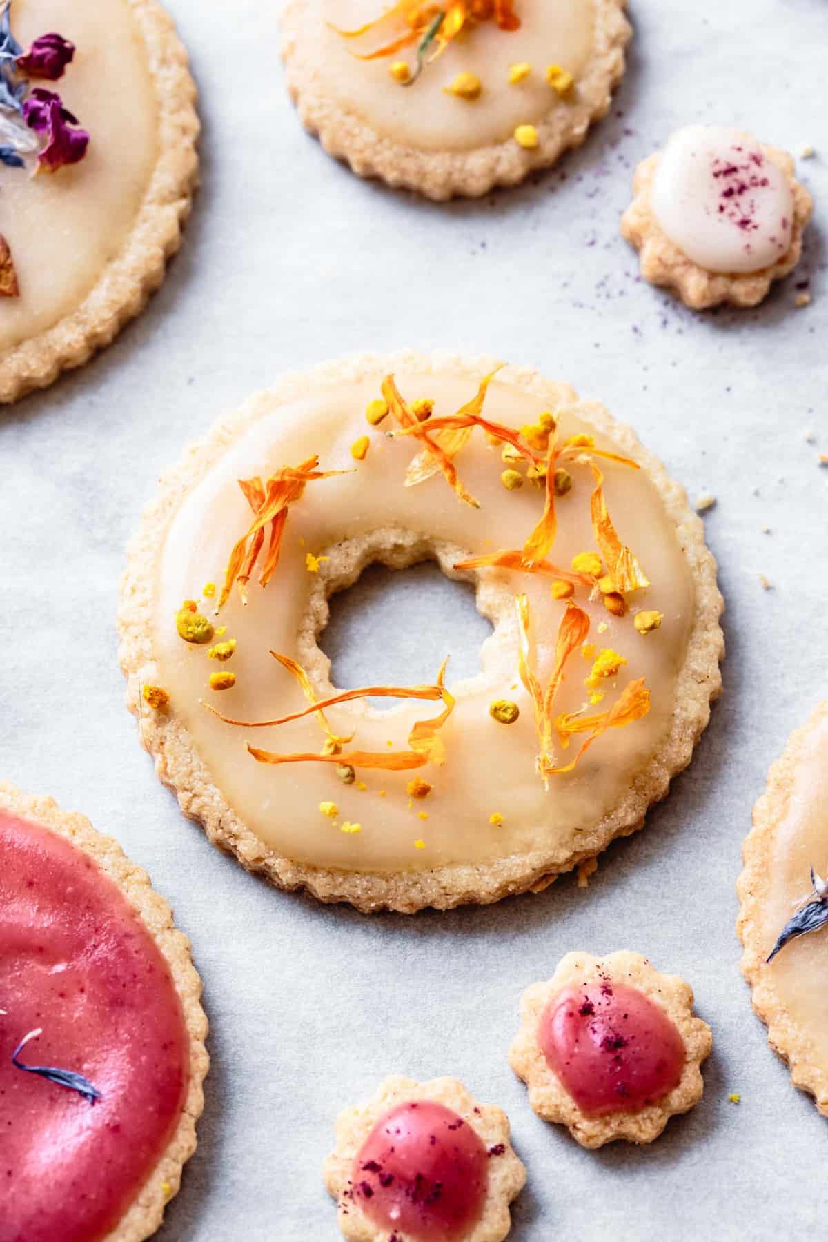 close-up of a gluten-free sugar cookie topped with icing, orange flower petals, and bee pollen