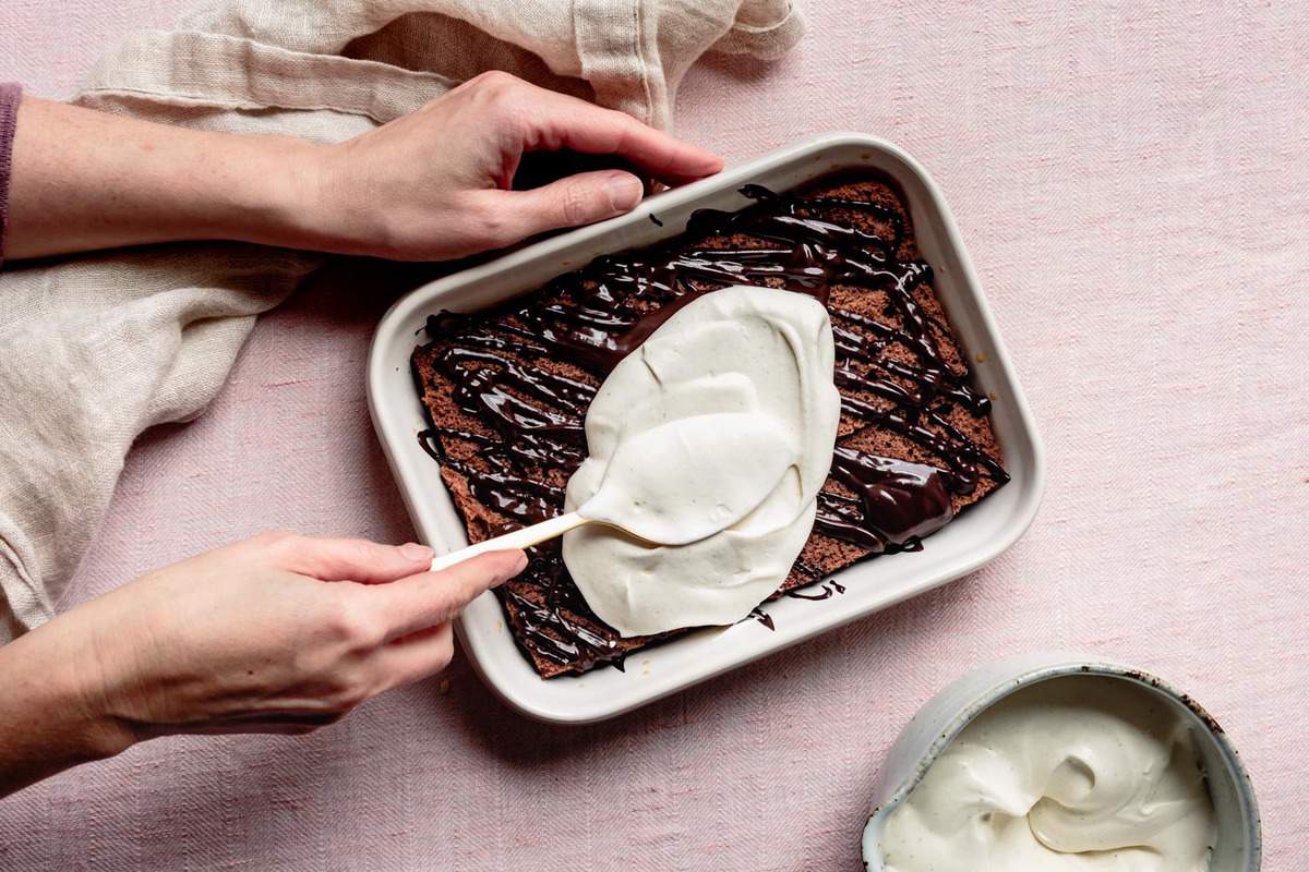 hands spreading whipped mascarpone over cake and nutella