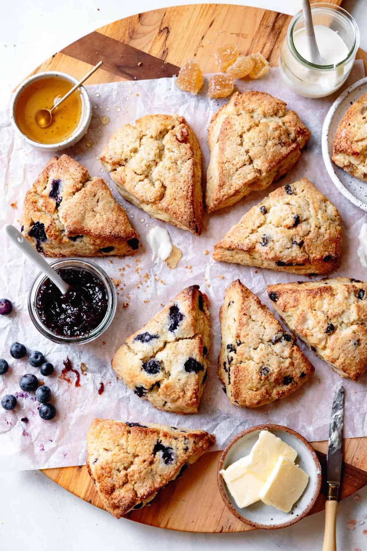 a variety of gluten-free scones on a large wooden board with honey, jam, and butter