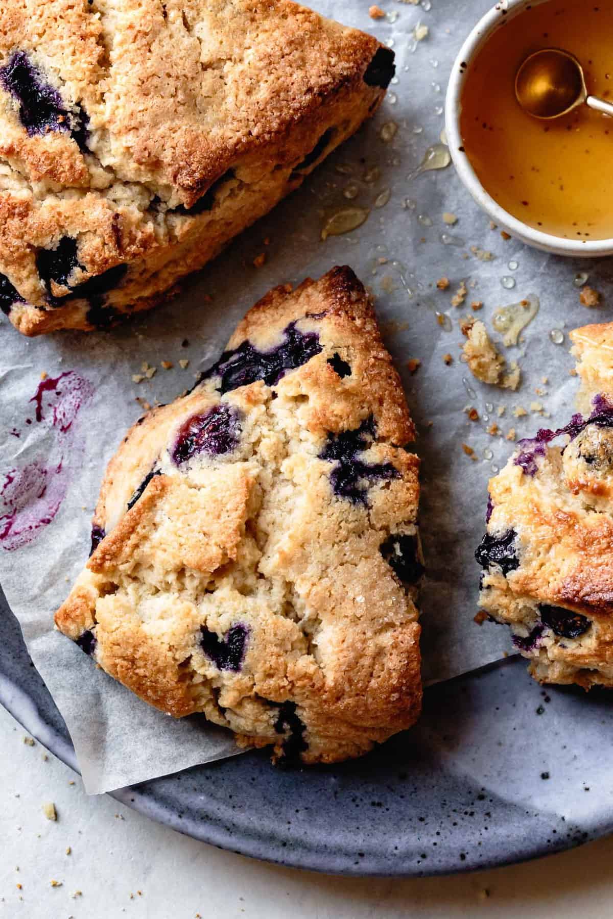 a gluten-free blueberry scone is on a parchment topped plate looking golden, craggy, and delicious