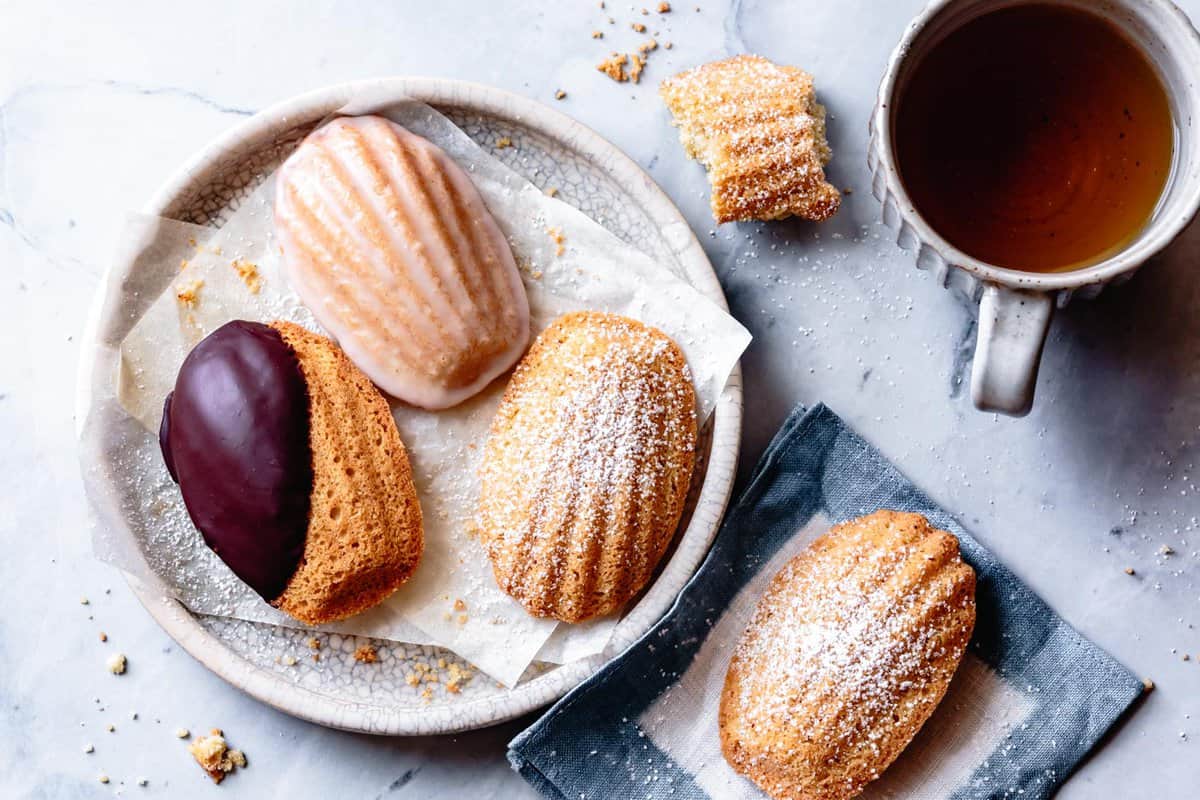 wide shot of three almond flour madeleines on a plate with different toppings and a cup of tea