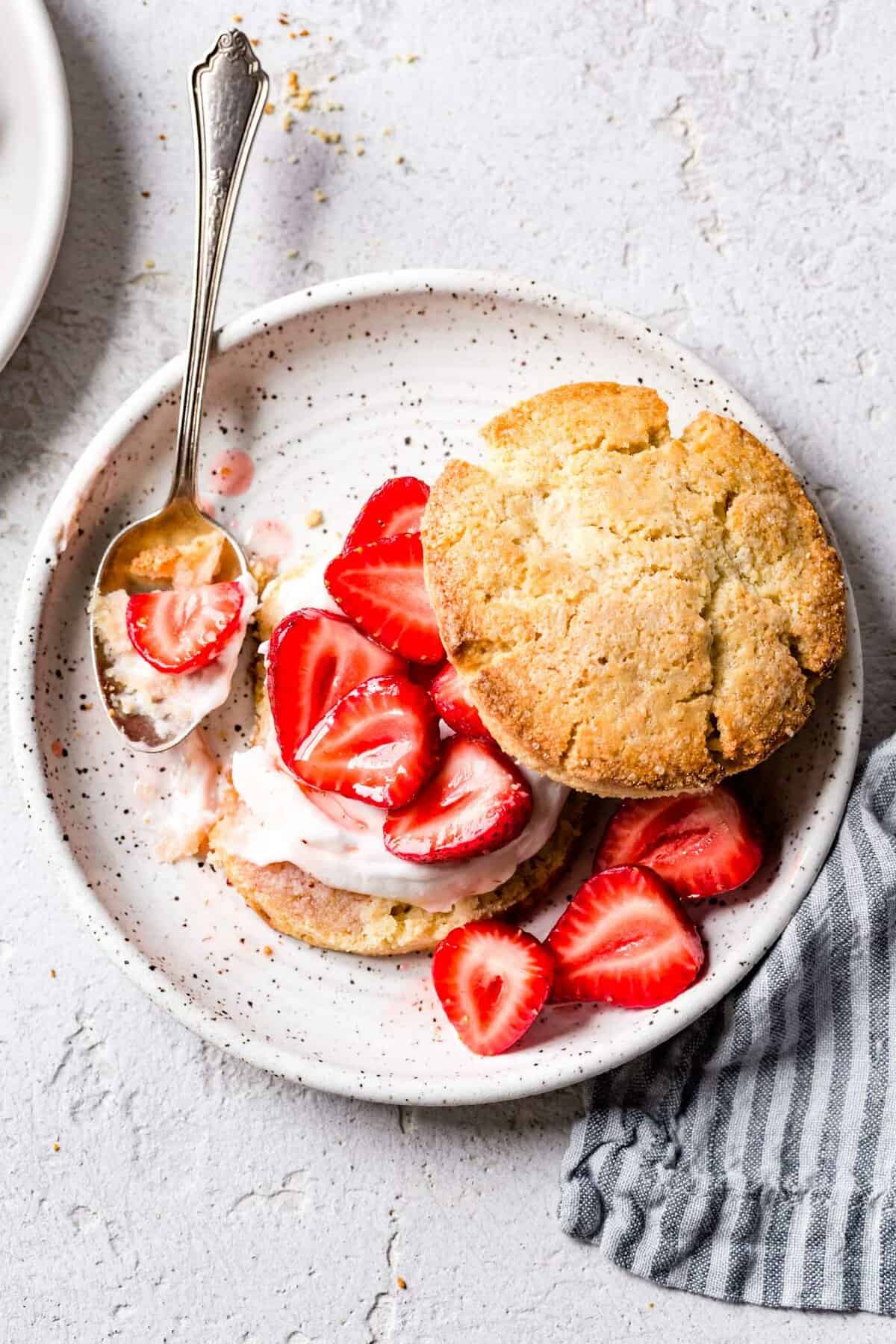 A gluten-free strawberry shortcake sits on a speckled plate with a spoonful taken out in a way that makes you want to dive right in!