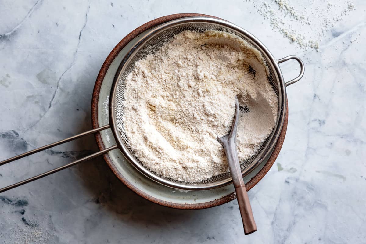 the flours are being sifted into a bowl