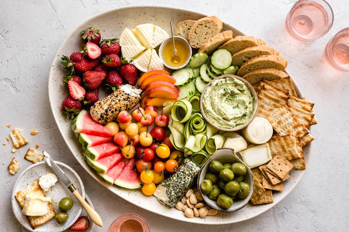 wide shot of cheese board on a plaster surface with pretty pink drinks alongside