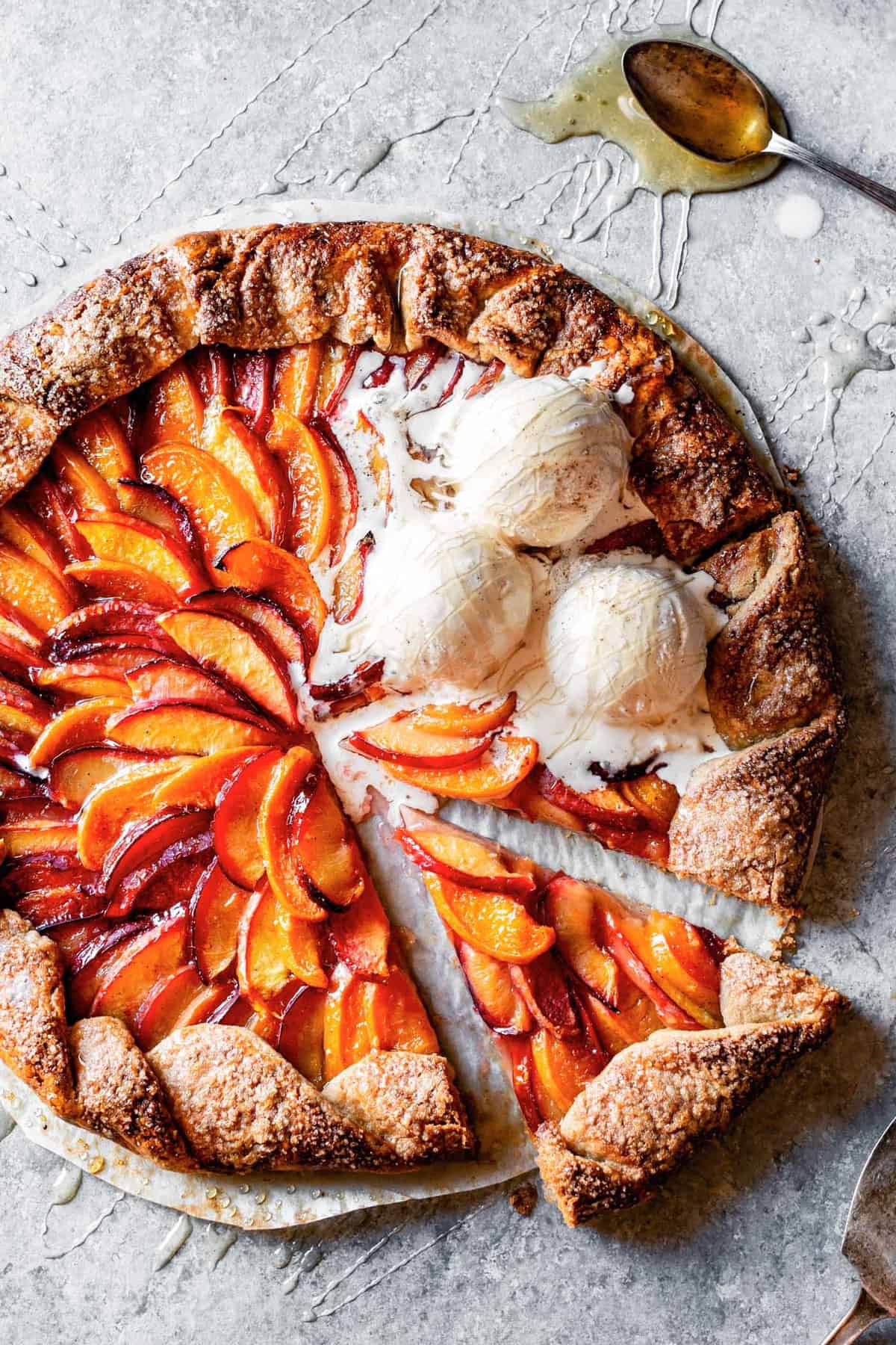 A gluten free stone fruit galette with two slices cut out, topped with scoops of drippy vanilla ice cream and drizzled with honey. 